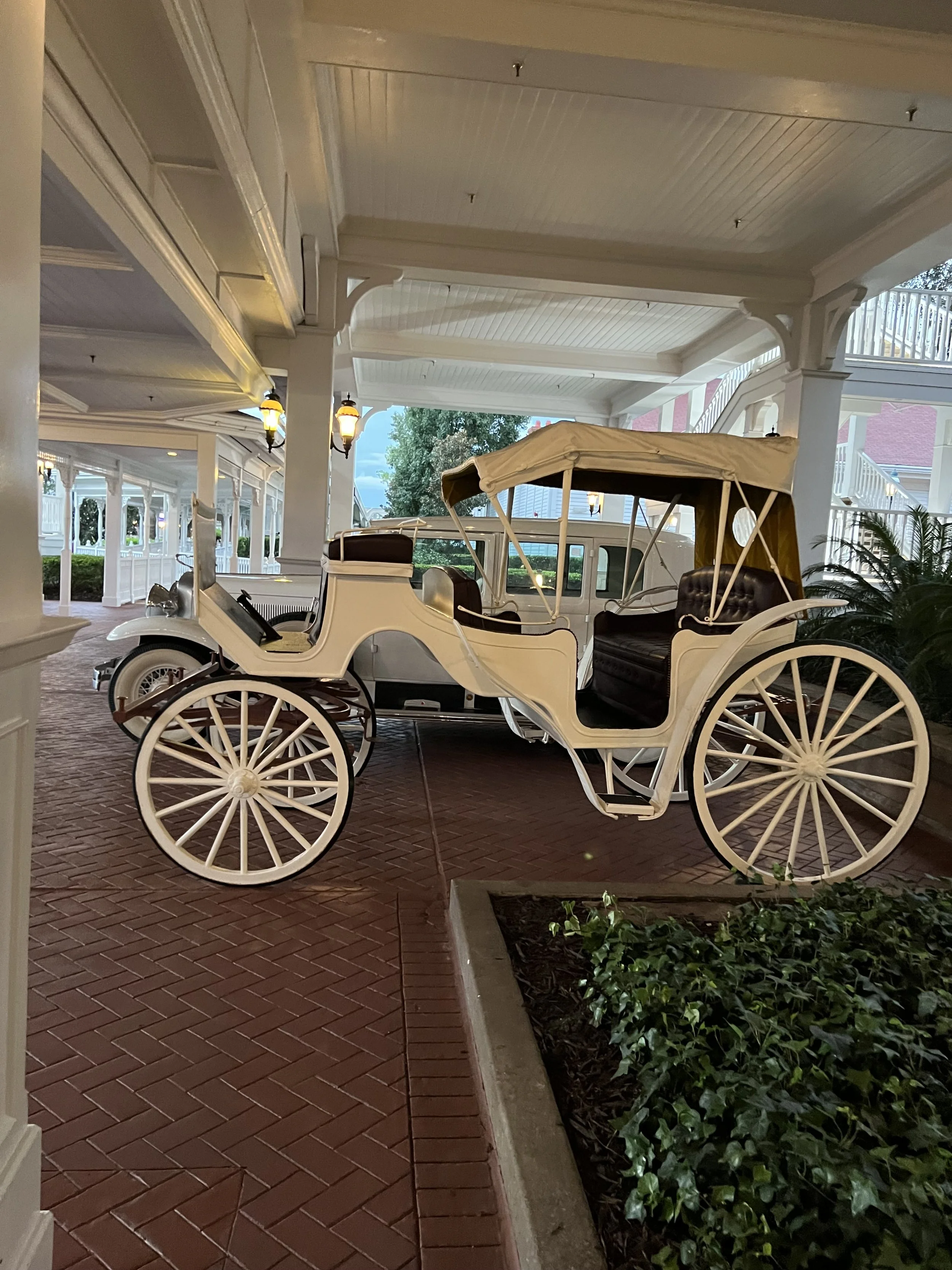 A vintage white horse-drawn carriage with black leather seats displayed under a covered porch area.