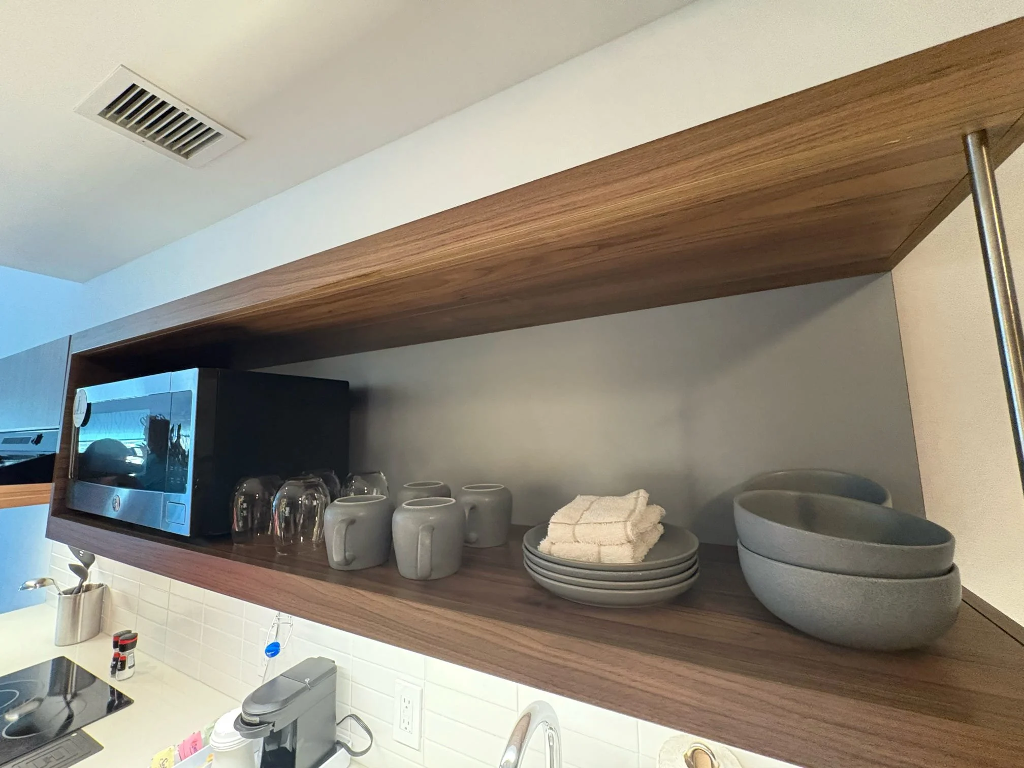 Open kitchen cabinet shelf with cups, bowls, and a microwave oven.