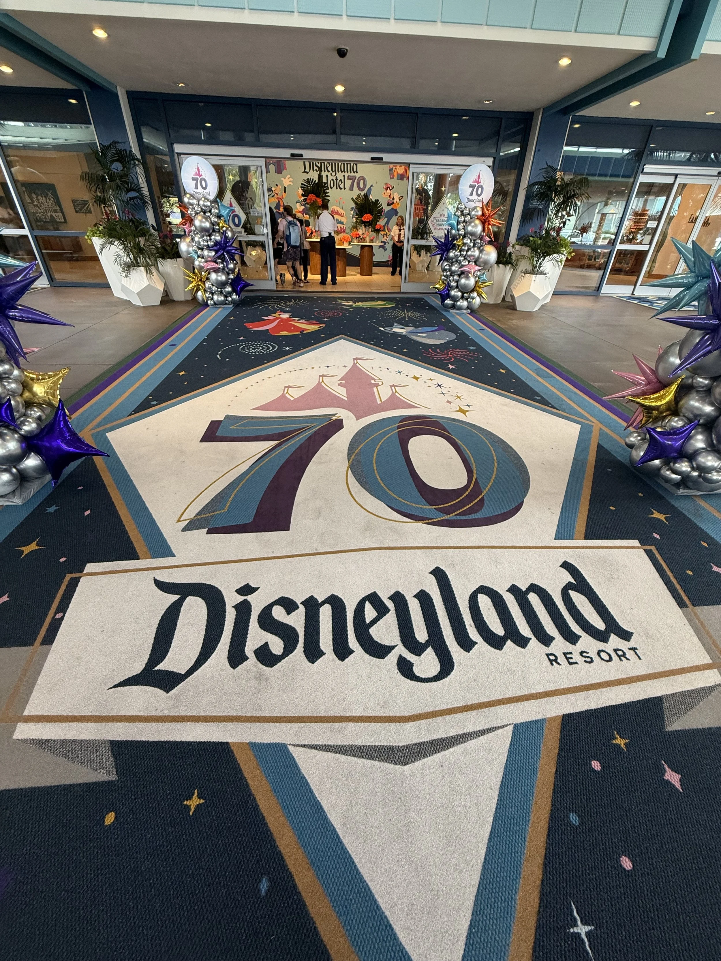 Entrance floor of Disneyland Resort decorated with large Disney-themed carpet featuring the number 70 and colorful stars, surrounded by balloon arrangements.