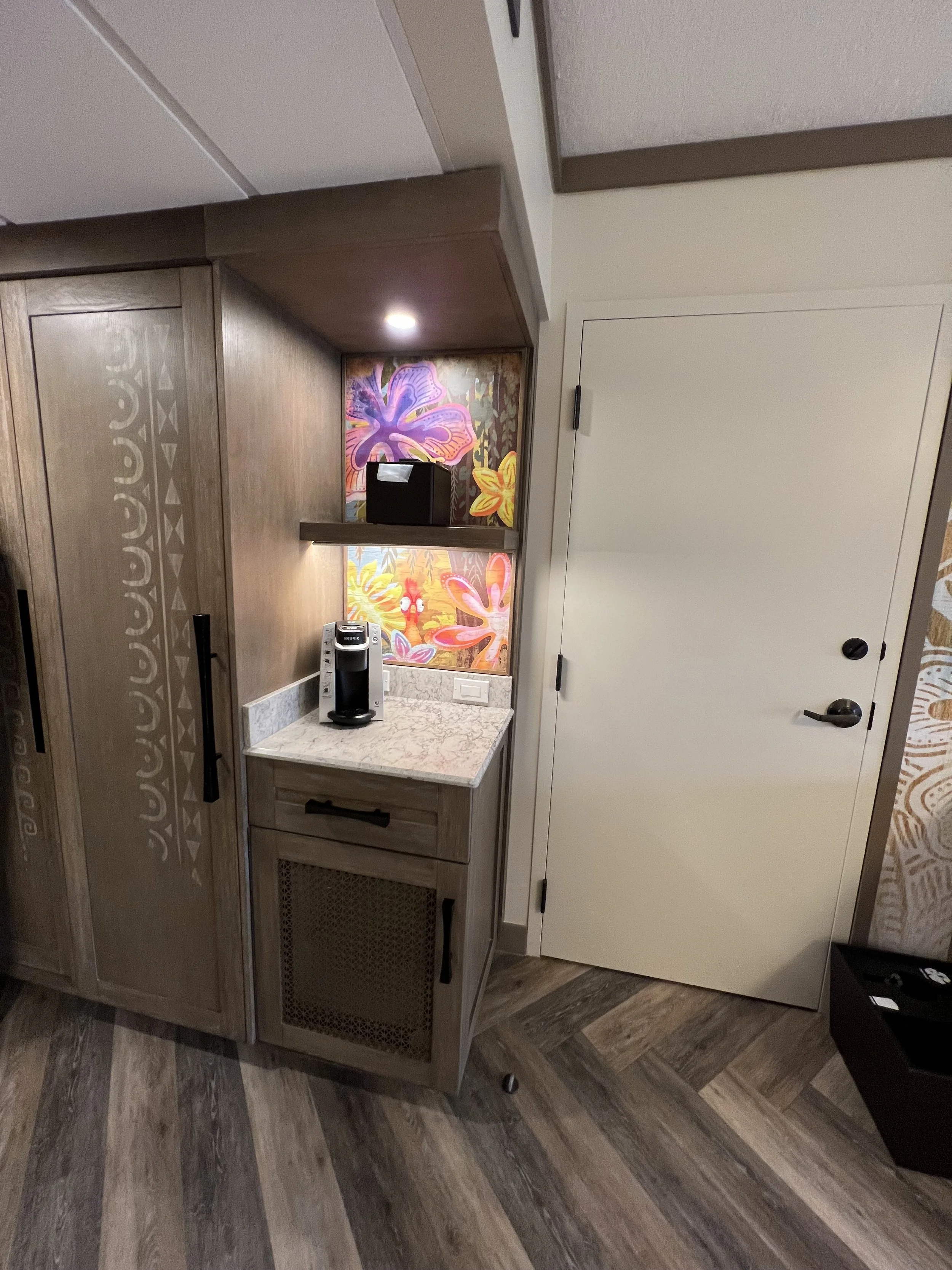 Small coffee station with a Keurig coffee maker on a marble countertop, decorated with colorful tropical floral wallpaper in the background, and a closed white door next to it.