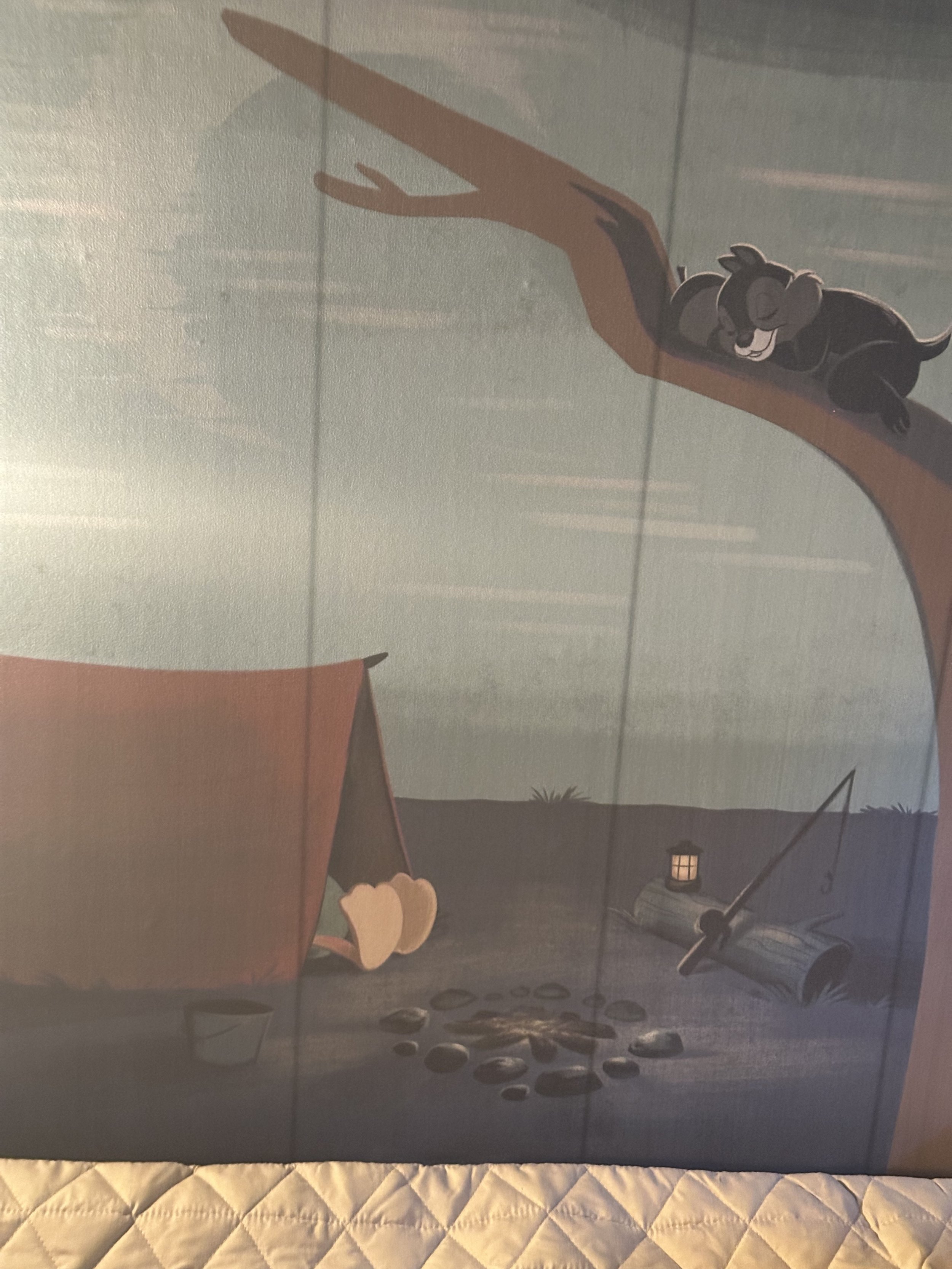 Cartoon image of a sleeping koala on a tree branch, a tent with a pair of feet sticking out, a campfire with rocks around it, and a fishing pole leaning against a log near a lantern at sunset.