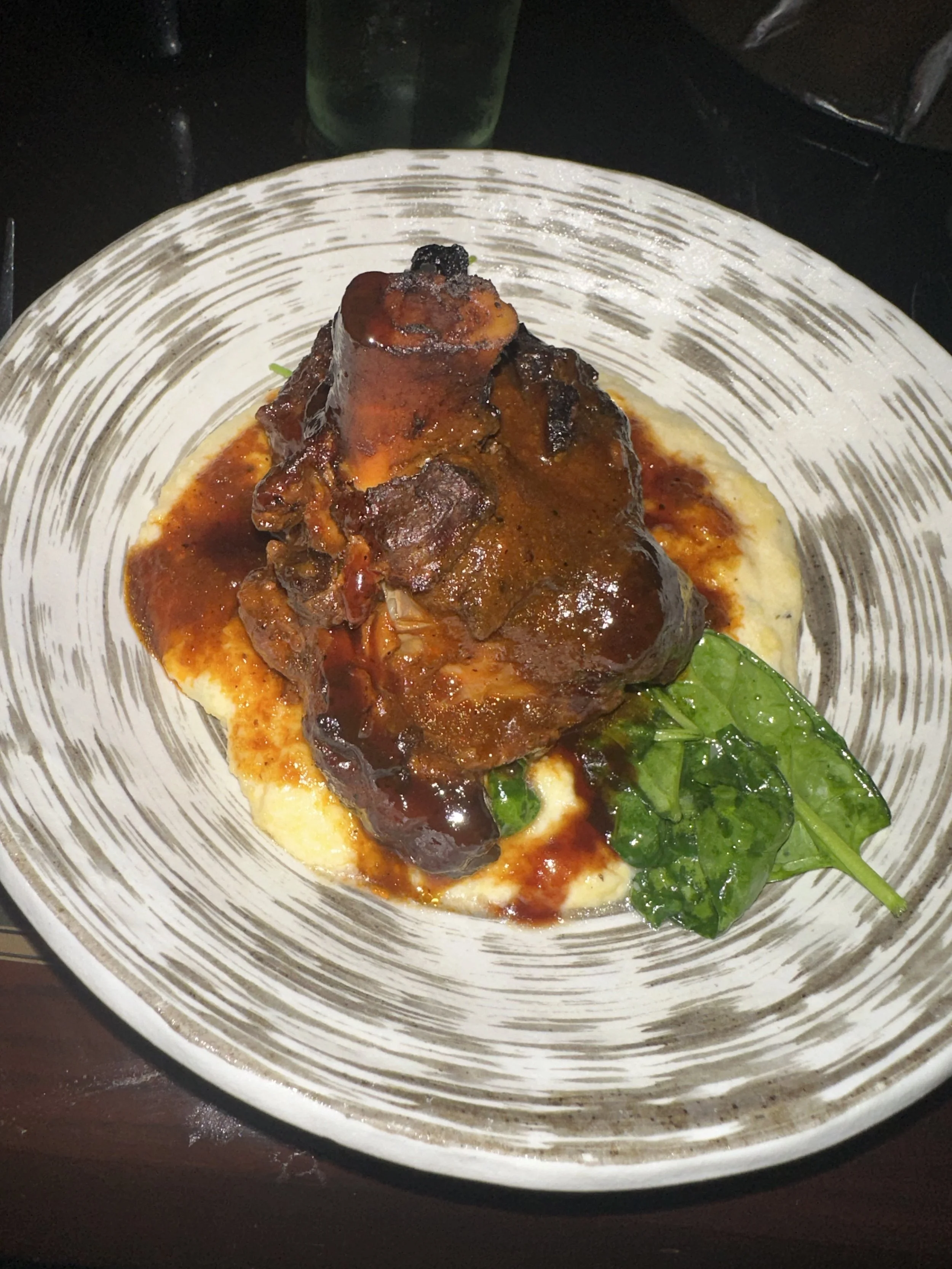A plated serving of braised beef short rib on mashed potatoes, garnished with spinach, with gravy sauce