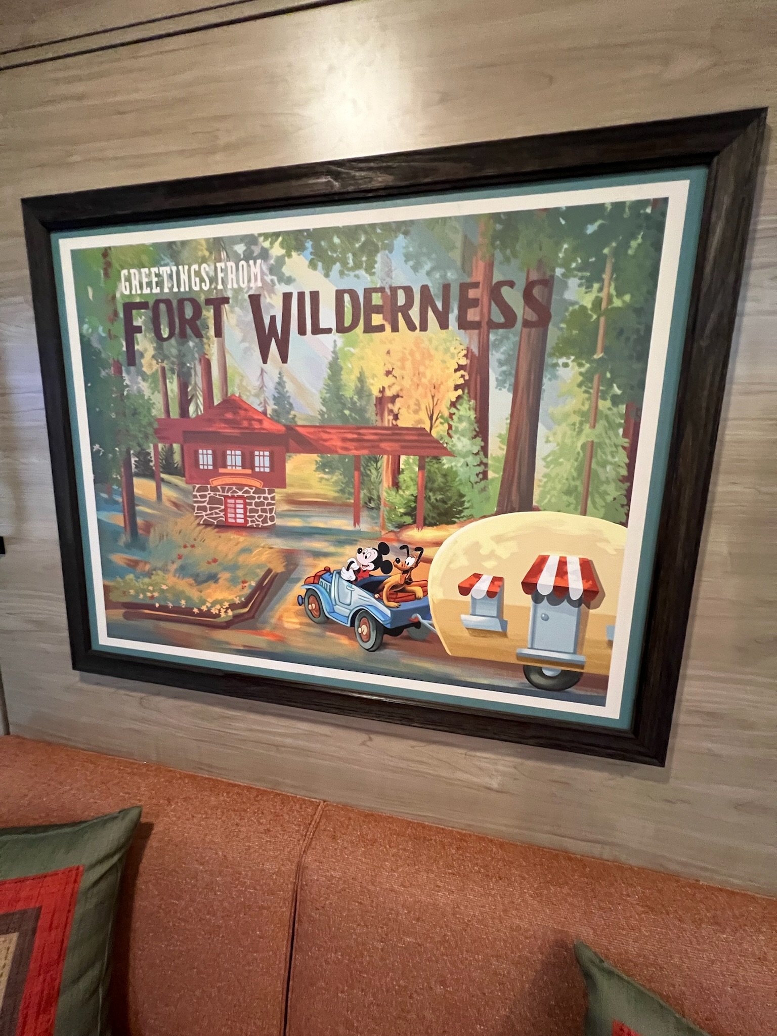 A colorful vintage-style illustration of a rustic cabin in a forest, with Mickey Mouse, Minnie Mouse, and Pluto riding a small blue car, and two mailboxes with red and white striped canopies, with the text "Greetings from Fort Wilderness."