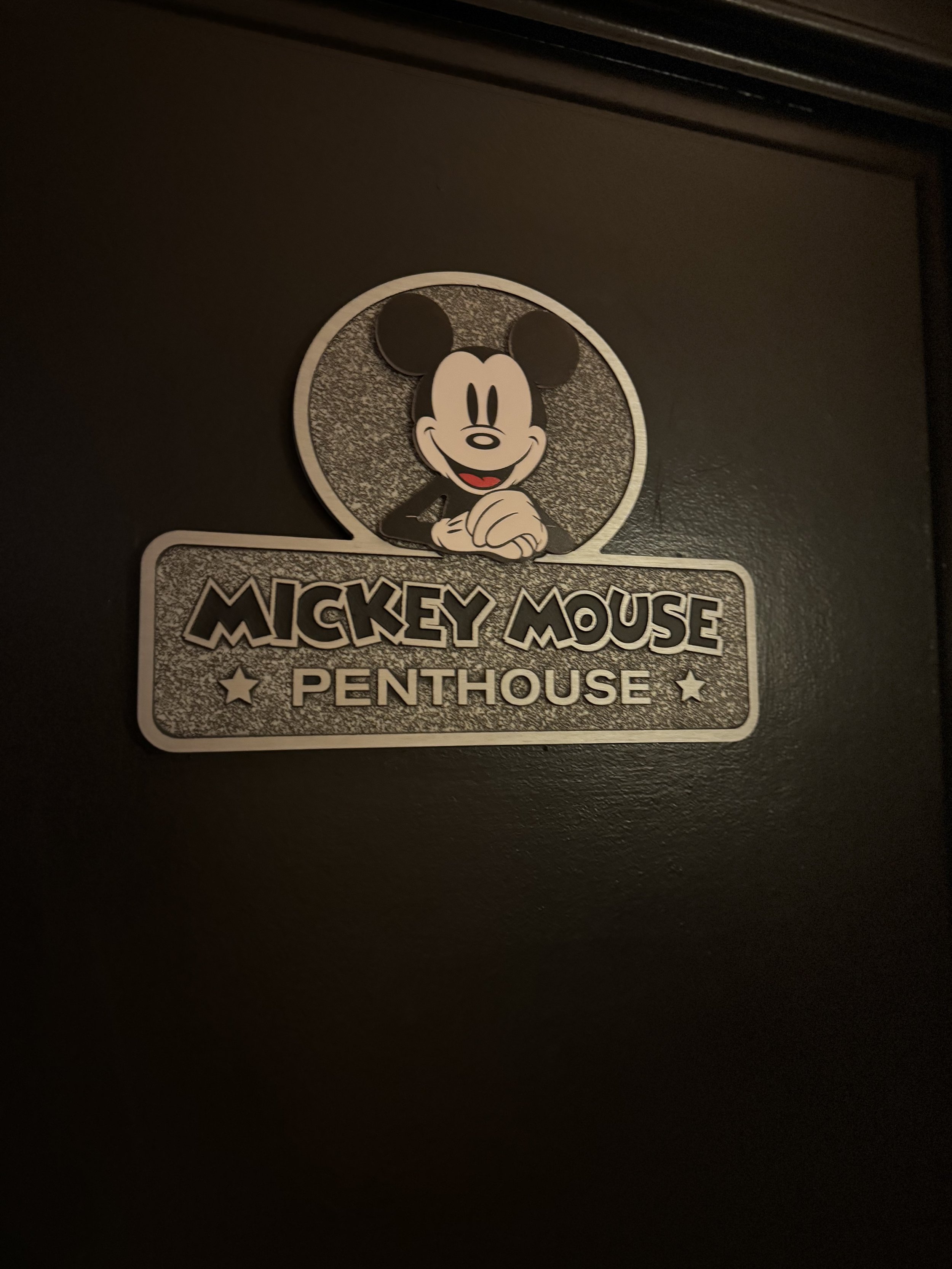 A sign with Mickey Mouse's face and arms, with the text "Mickey Mouse Penthouse" below it, mounted on a dark wall.