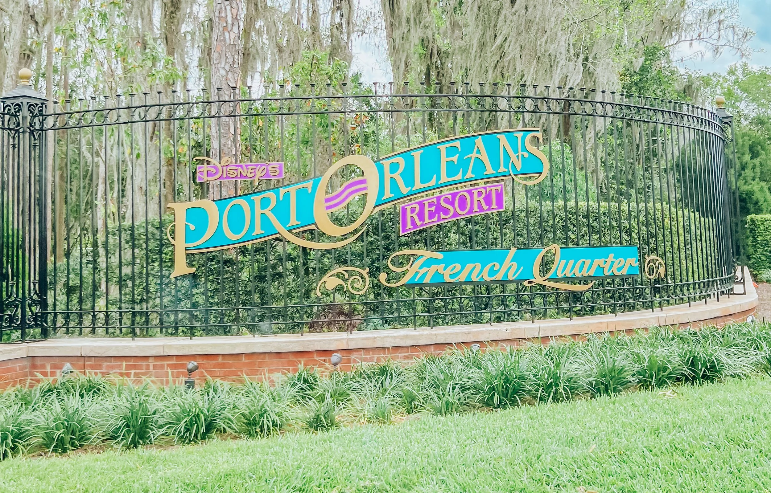 Entrance sign for Disney's Port Orleans Resort - French Quarter, with black wrought iron fence, green foliage, and Spanish moss in the background.