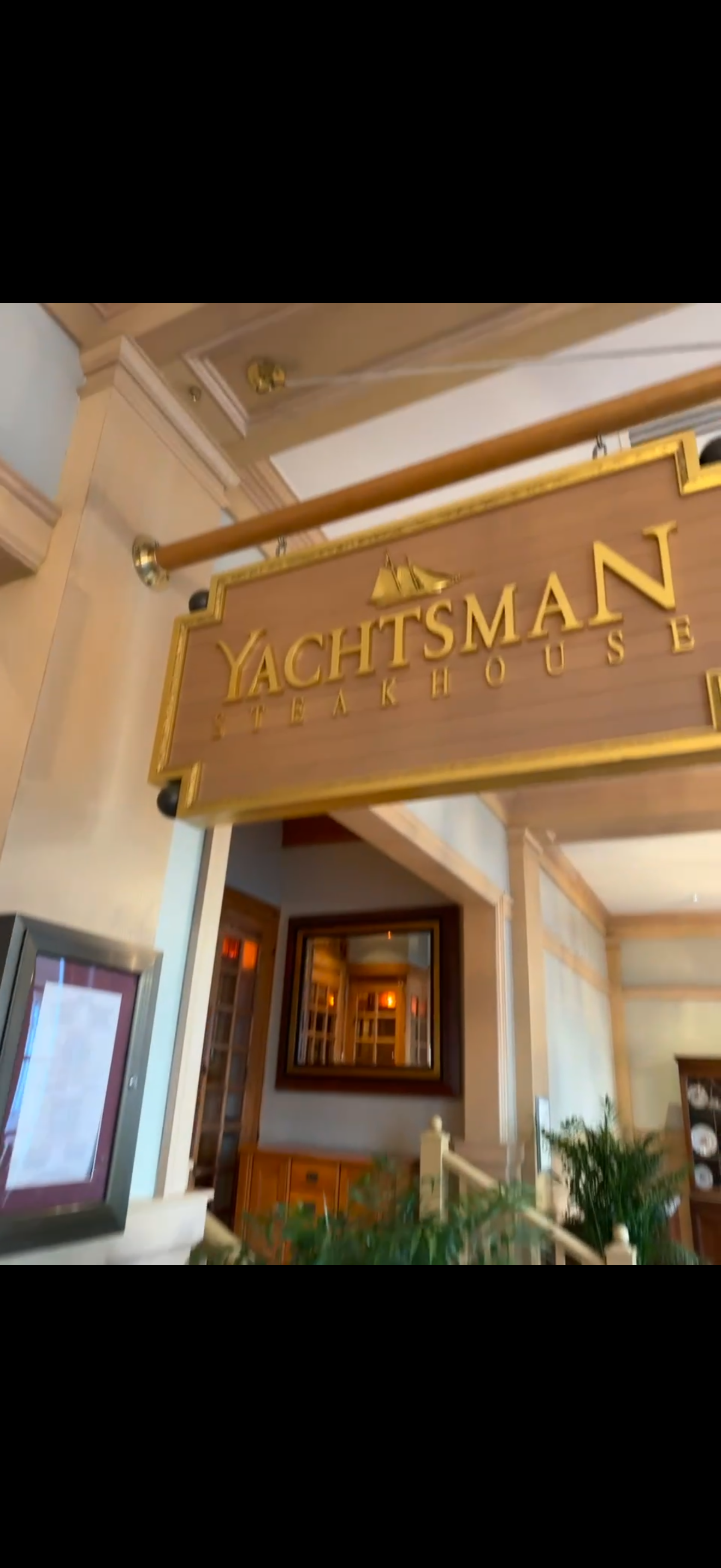 Wooden sign hanging inside a restaurant reads 'Yachtsman Steakhouse' with a small sailboat icon above the text.