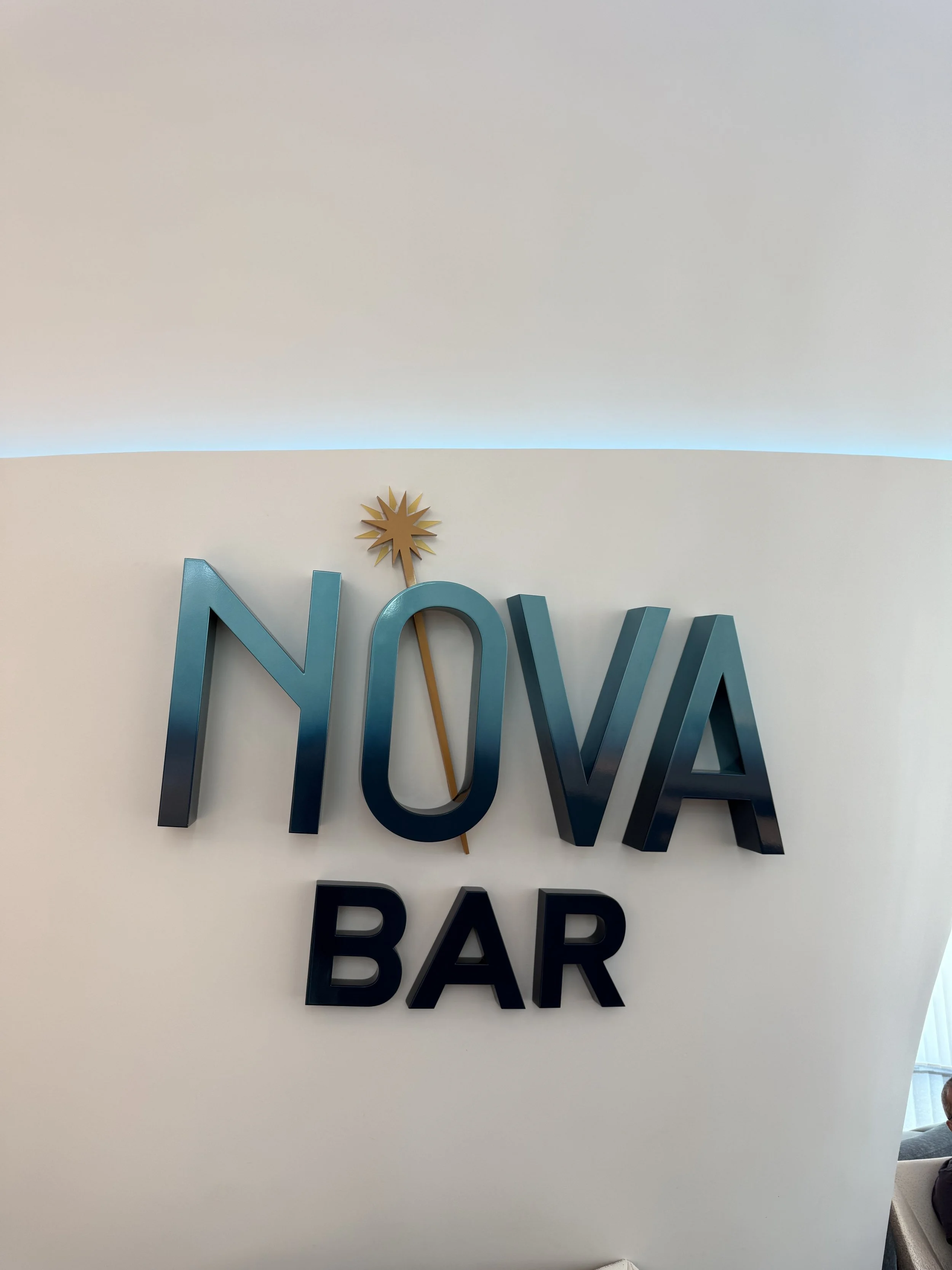 Sign for Noya Bar with a sunburst design above the letter O on a white wall.