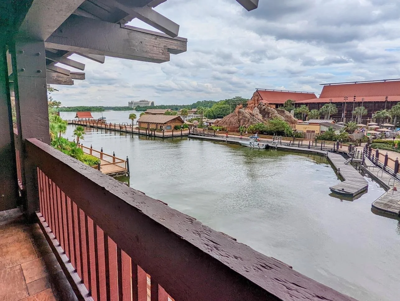 View of a lake or lagoon with docks, boats, and surrounding buildings, seen from a balcony with a wooden railing.