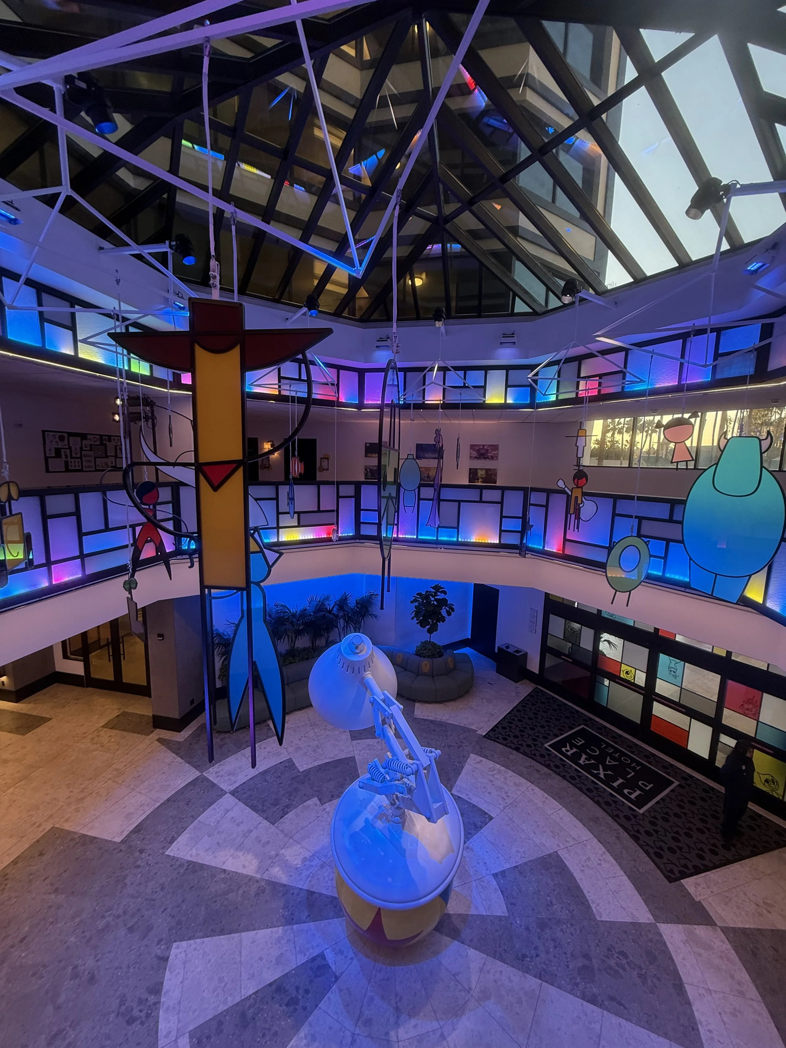 Indoor space themed like Andy Warhol's art with colorful neon-inspired artwork and sculptures, featuring a large robotic arm and a circular seating area, illuminated by multicolored lighting.