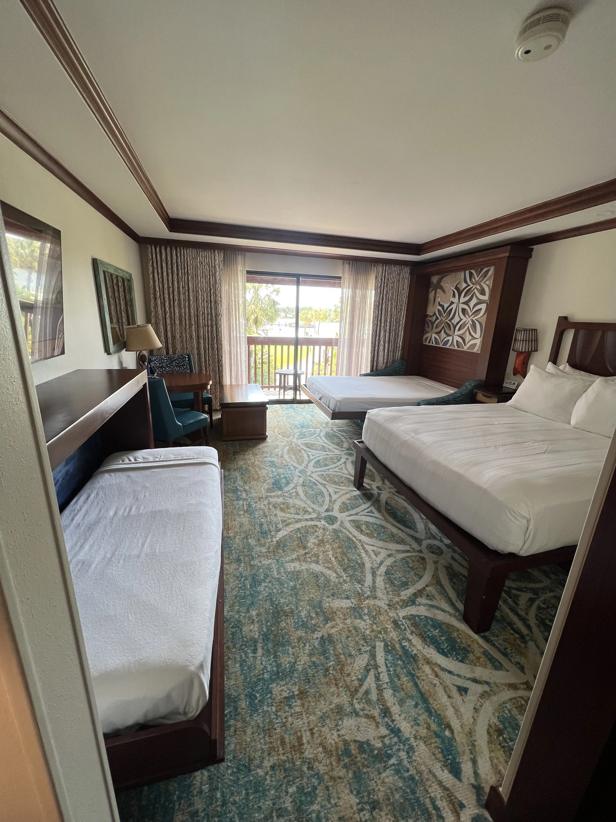 Hotel room with two beds, a sitting area near a sliding glass door, and a patterned rug.