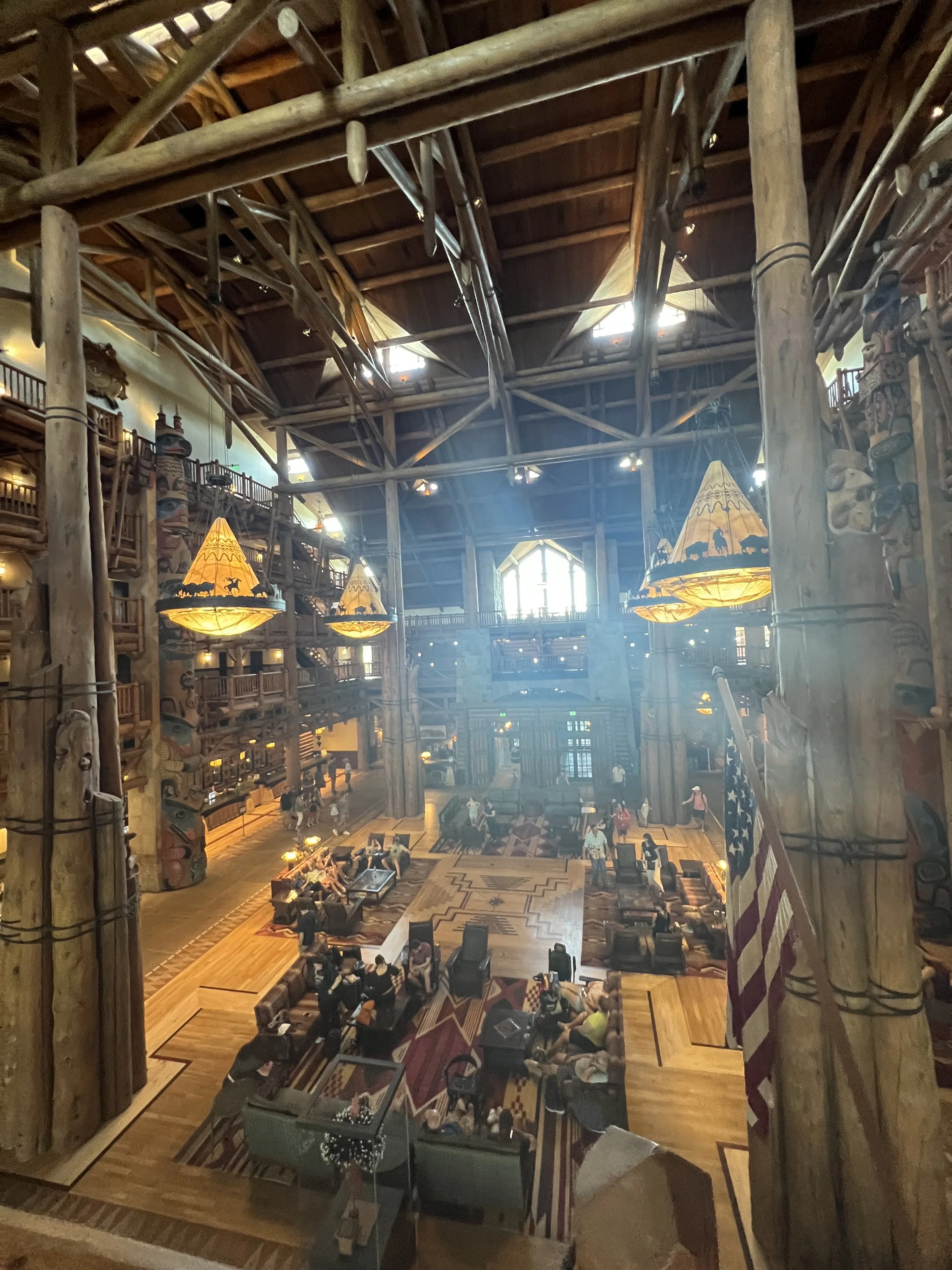 Interior of a large lodge with a high wooden ceiling, multiple hanging lamps, and a spacious seating area filled with people.