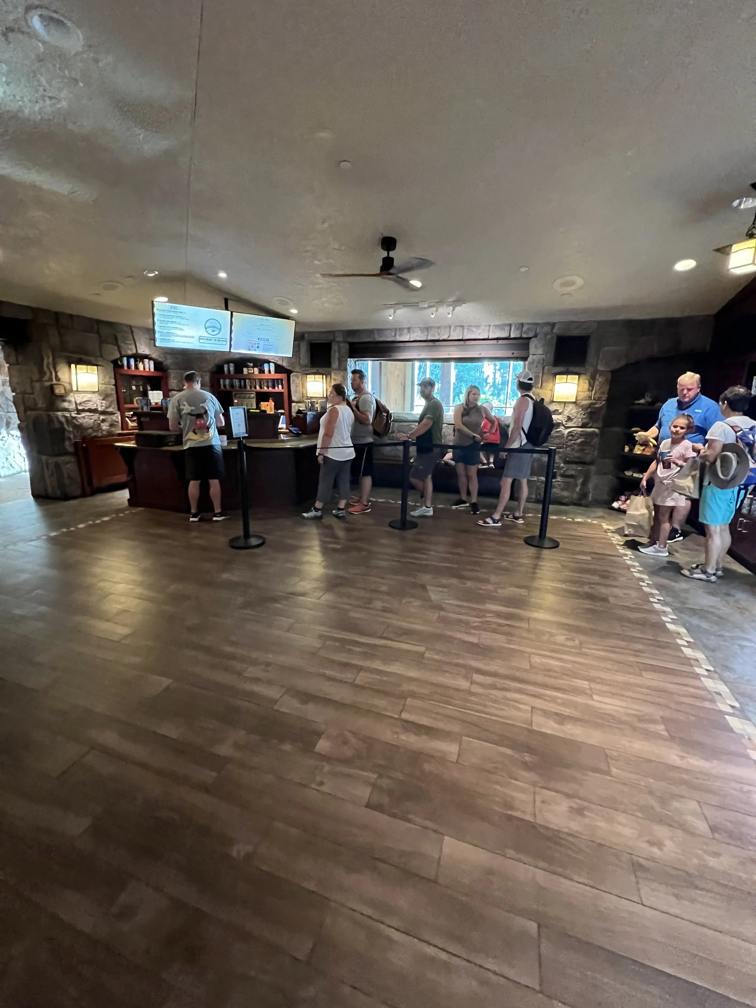 People standing in line at a service counter inside a building with stone walls and wooden flooring.