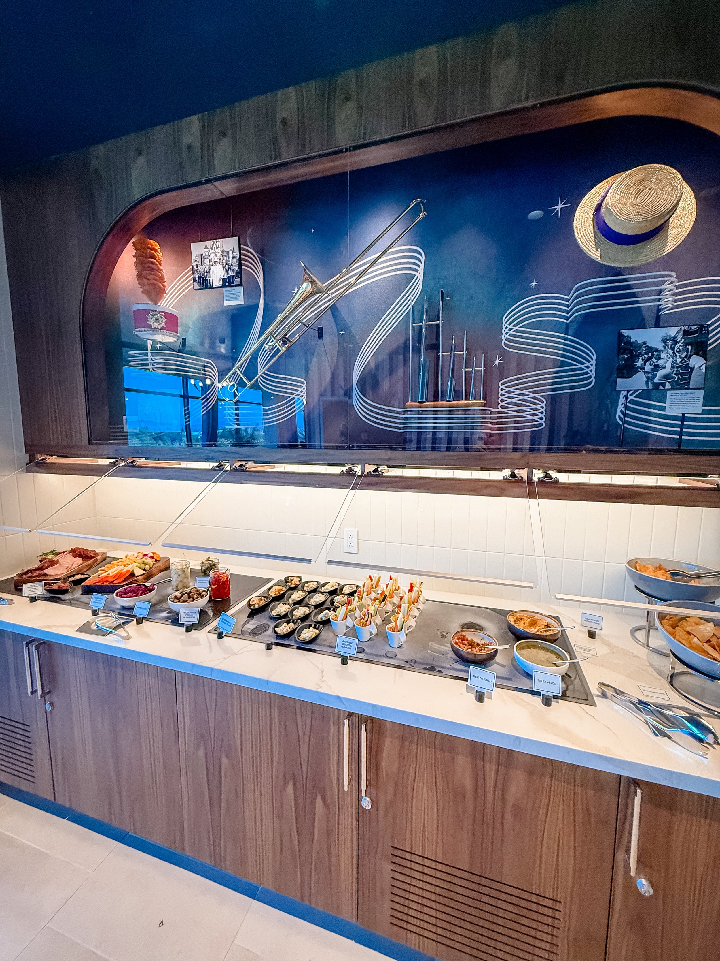 Buffet table with various condiments, vegetables, and sauces in bowls, with a vintage musical instrument display in the background.