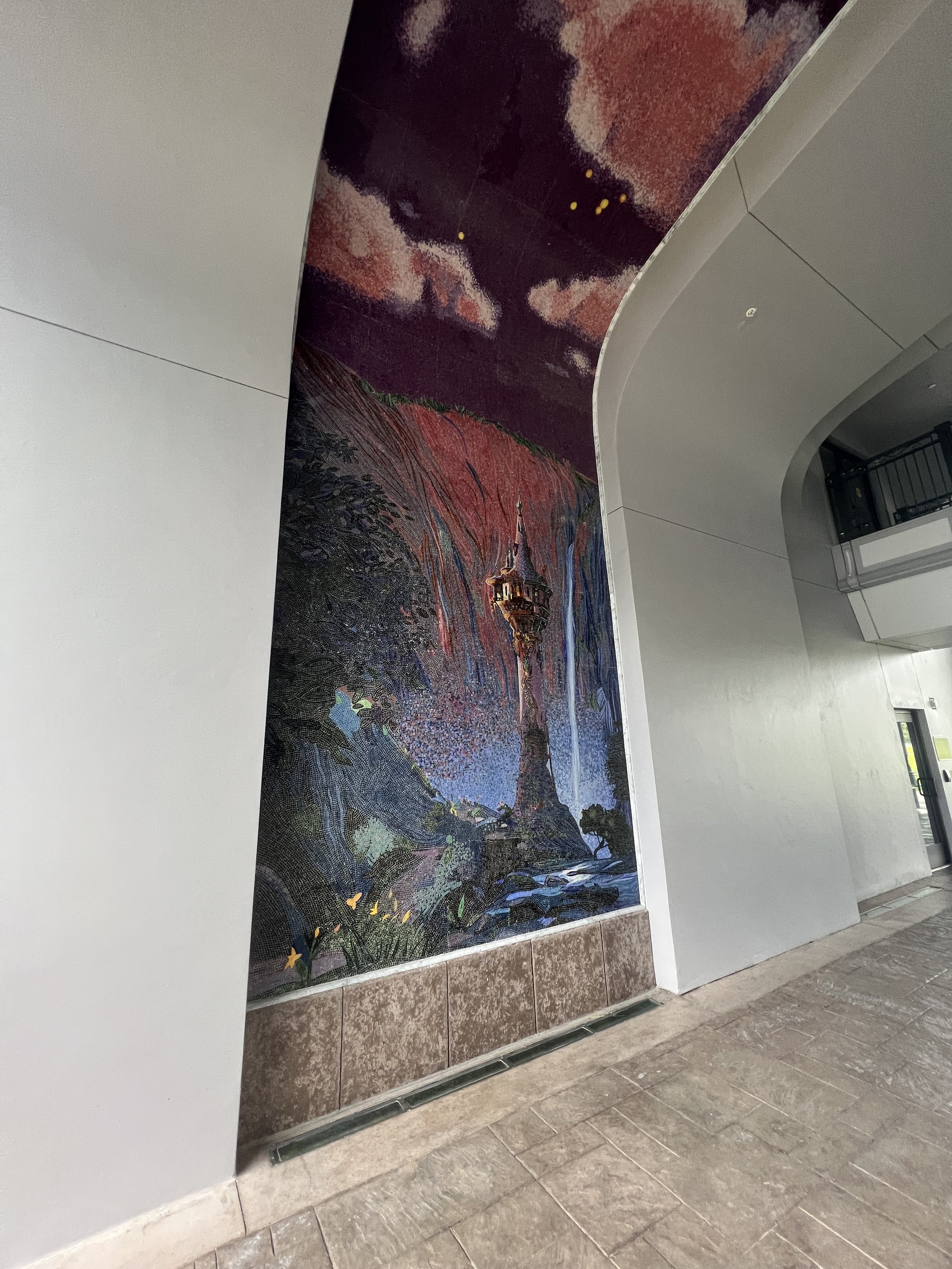 Colorful mural of a theme park tower with a sunset sky, trees, and butterflies on a wall inside a building.