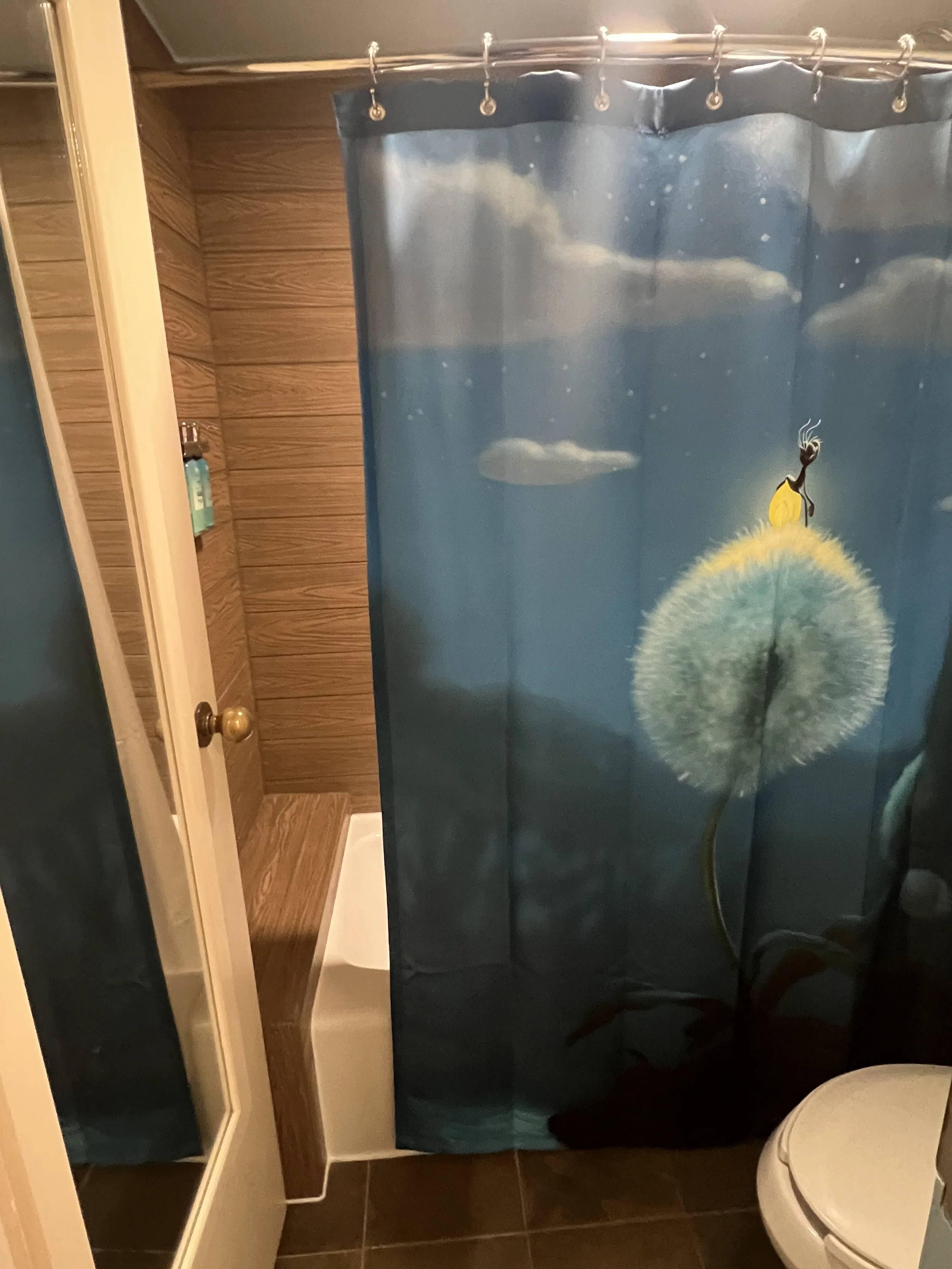 Bathroom shower curtain with a dandelion design, partially revealing a shower area with wooden walls and a white shower base.