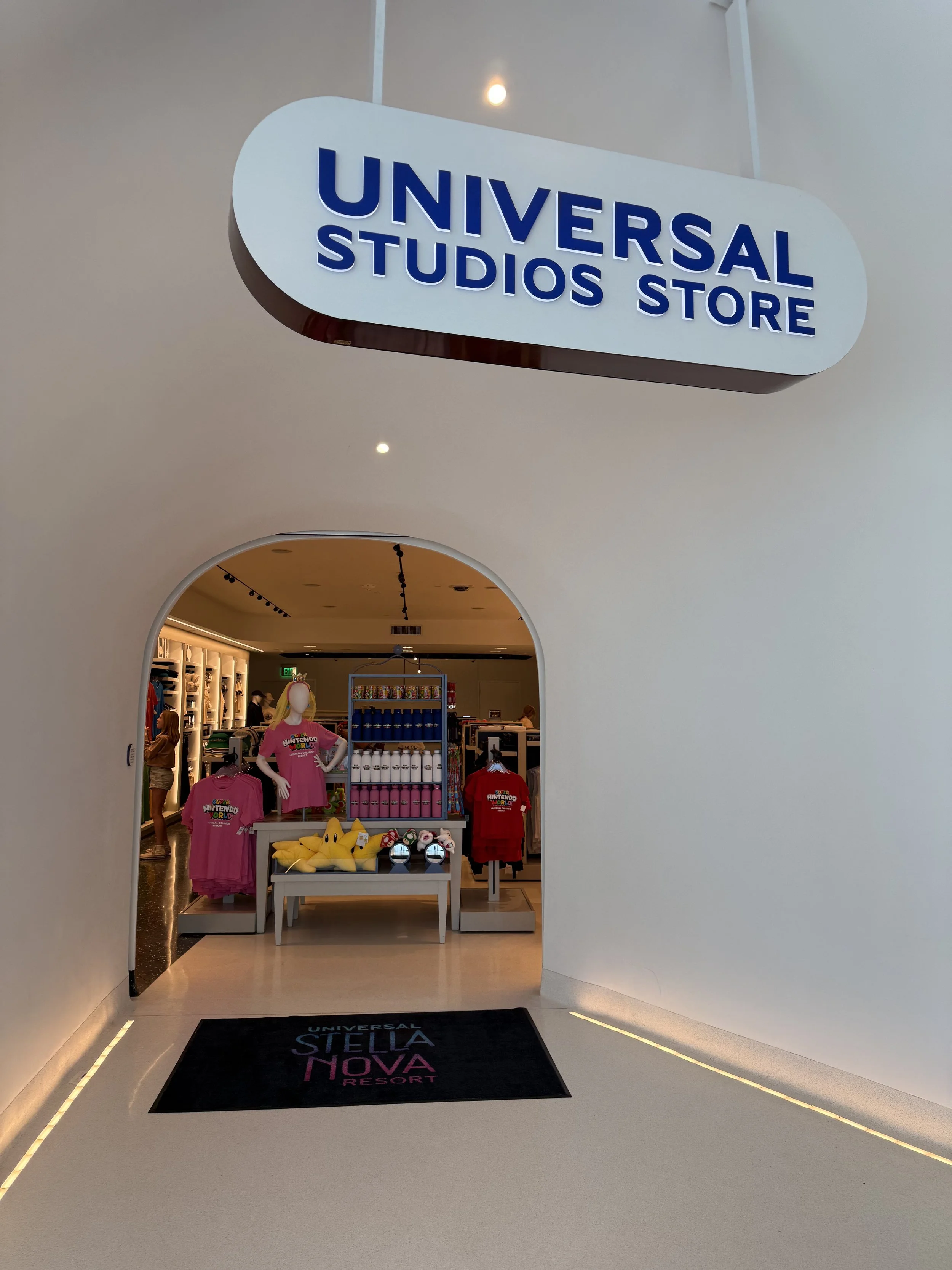 Entrance to the Universal Studios Store at Universal's Stella Nova Resort, with merchandise including shirts, plush toys, and water bottles visible inside.