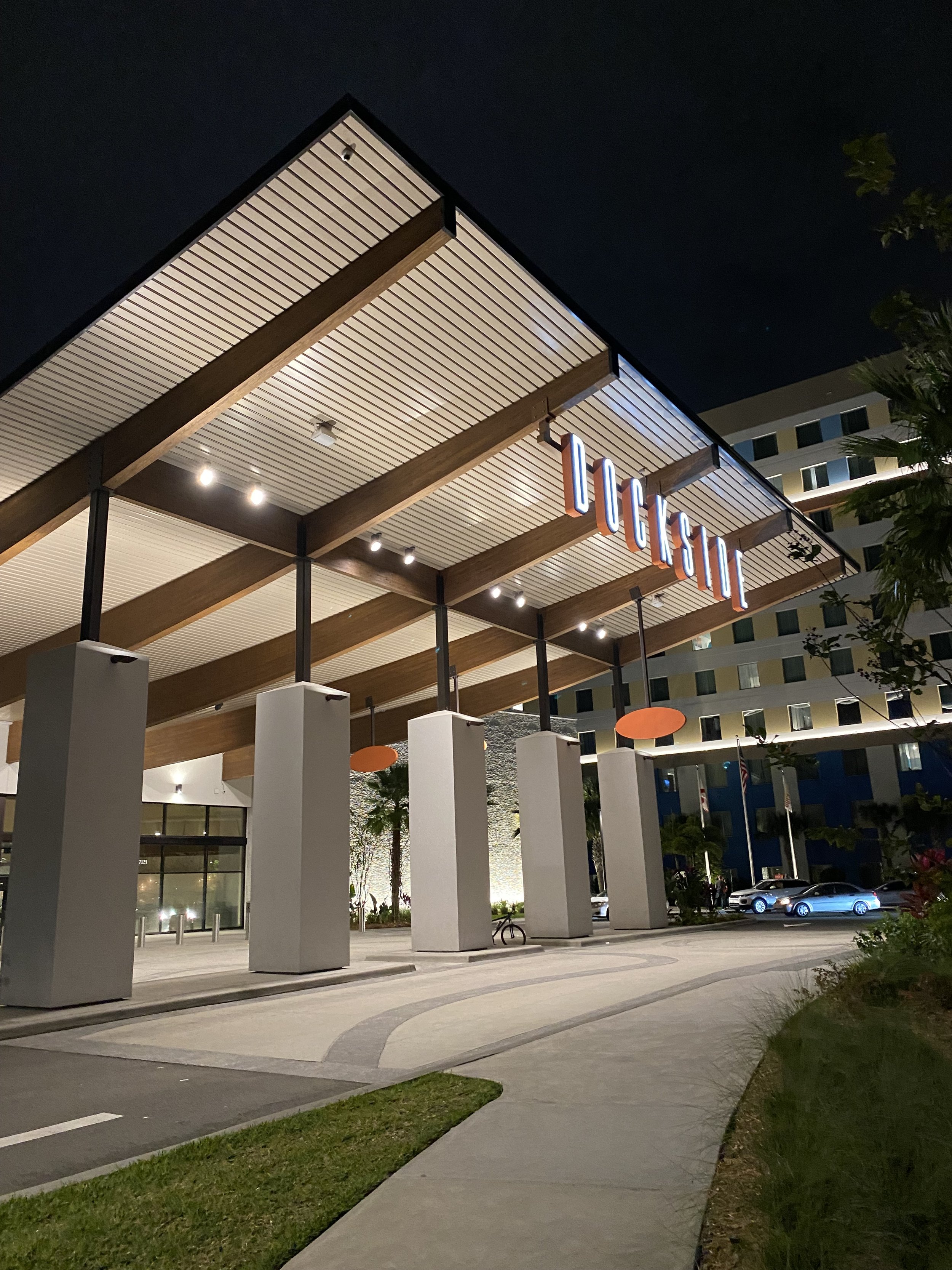 Nighttime exterior view of a modern building with a large illuminated sign reading 'LUGUHI' under a wooden and metal canopy.