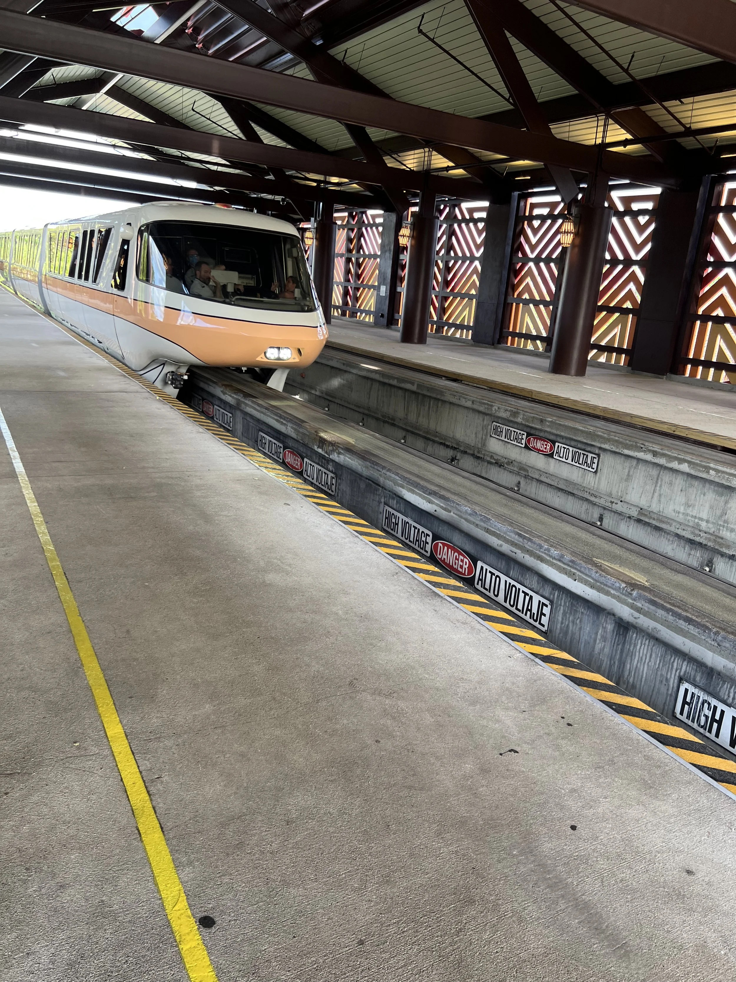 A NASA tram on an elevated track at a transportation station with signs warning of high voltage and danger.