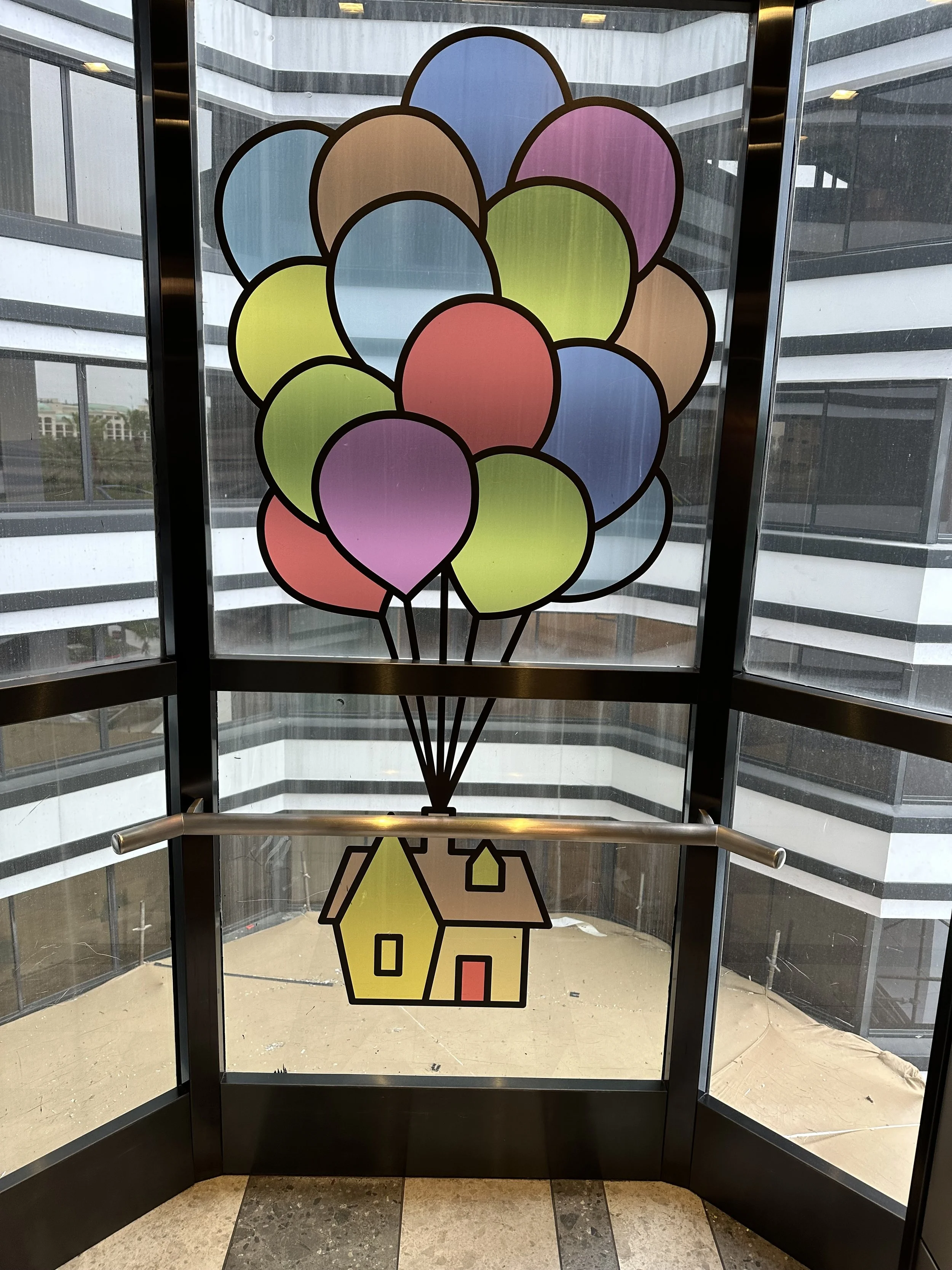 Colorful sticker of balloons tied to a house on elevator door glass.