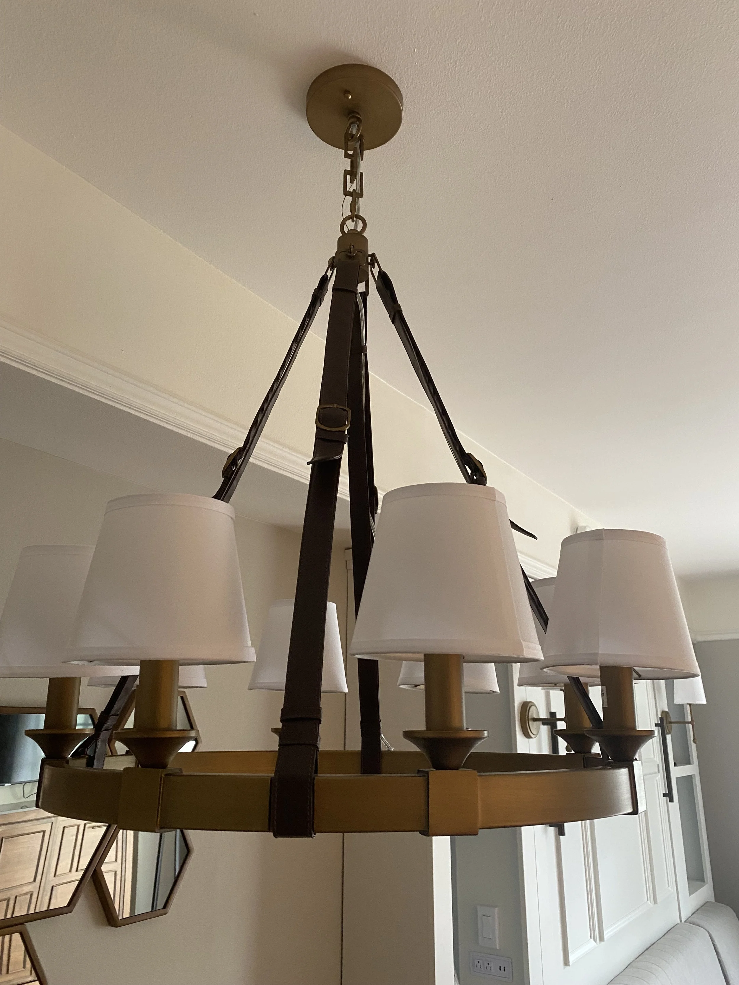 A chandelier with six light fixtures and white lampshades hanging from a ceiling in a room.