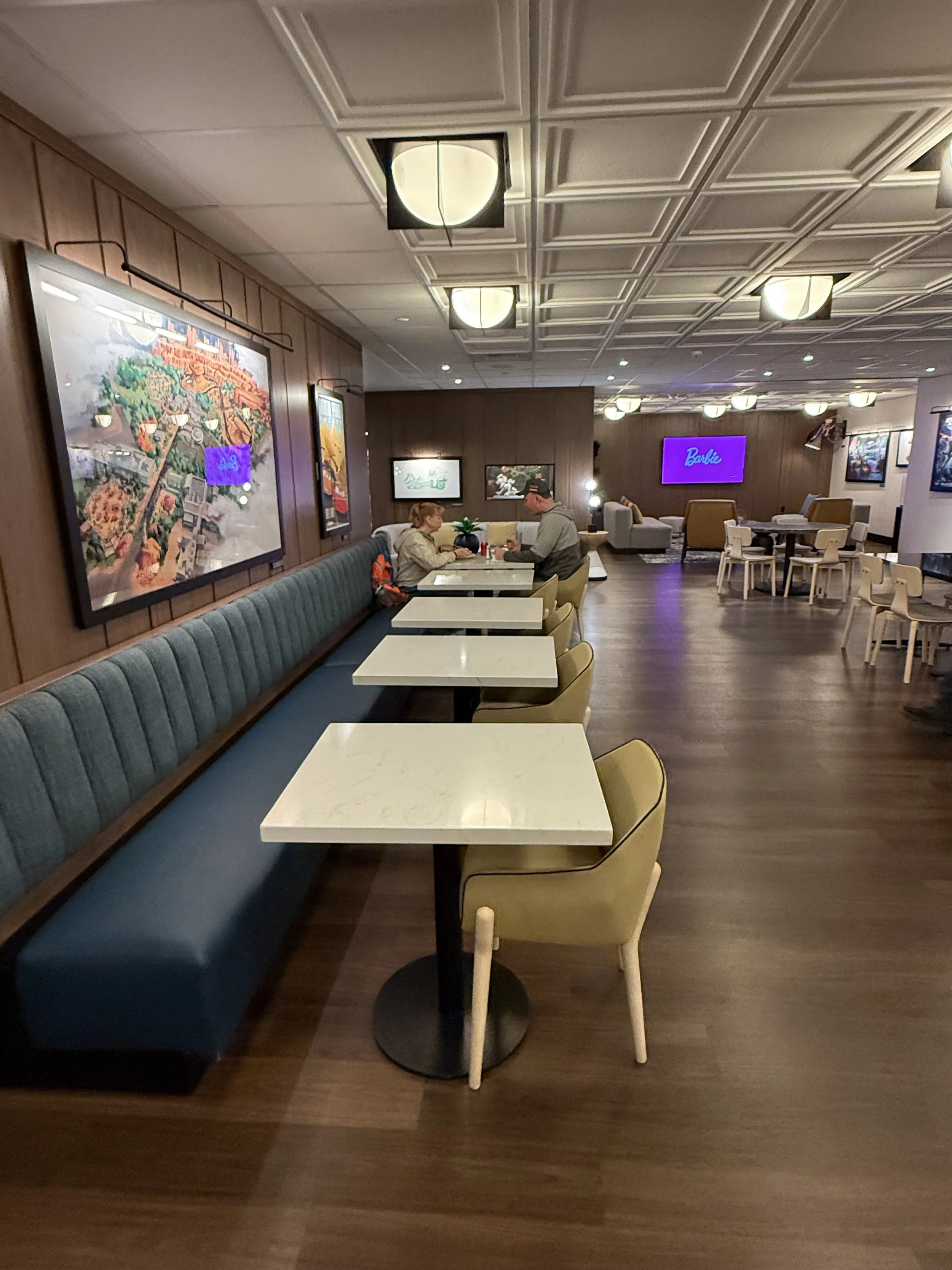 Empty restaurant with a few people sitting at a table, decorated with framed artwork on wood-paneled walls, and a large 