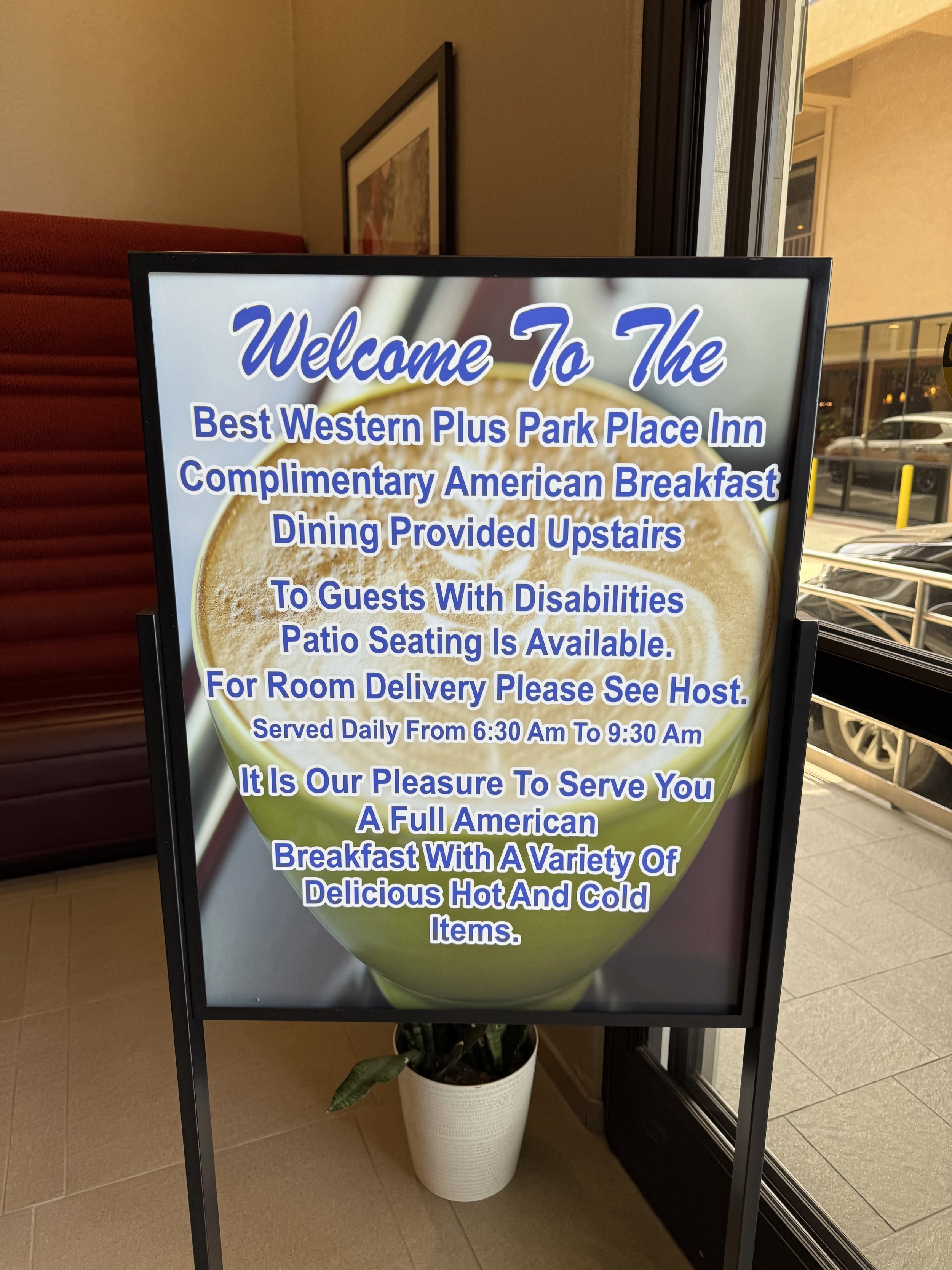 A digital sign welcoming guests to the Best Western Plus Park Place Inn with information about complimentary American breakfast served daily from 6:30 am to 9:30 am, available upstairs, with patio seating, room delivery, and a variety of hot and cold