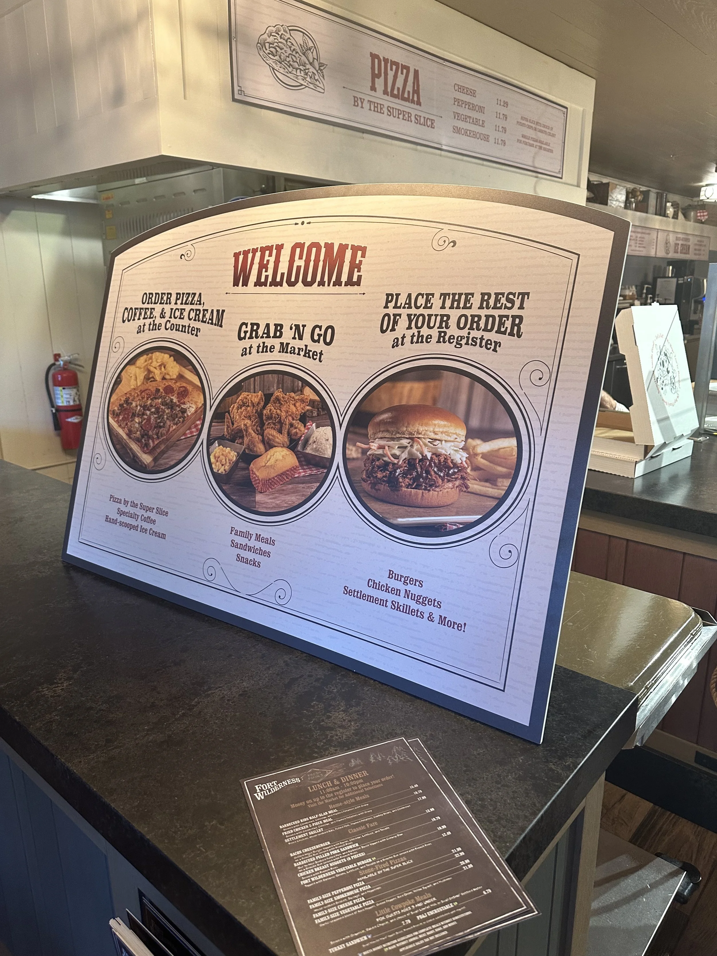 Restaurant menu board featuring options like pizza, grab 'n go meals, and in-restaurant ordering with images of pizza, fried chicken, and a burger.