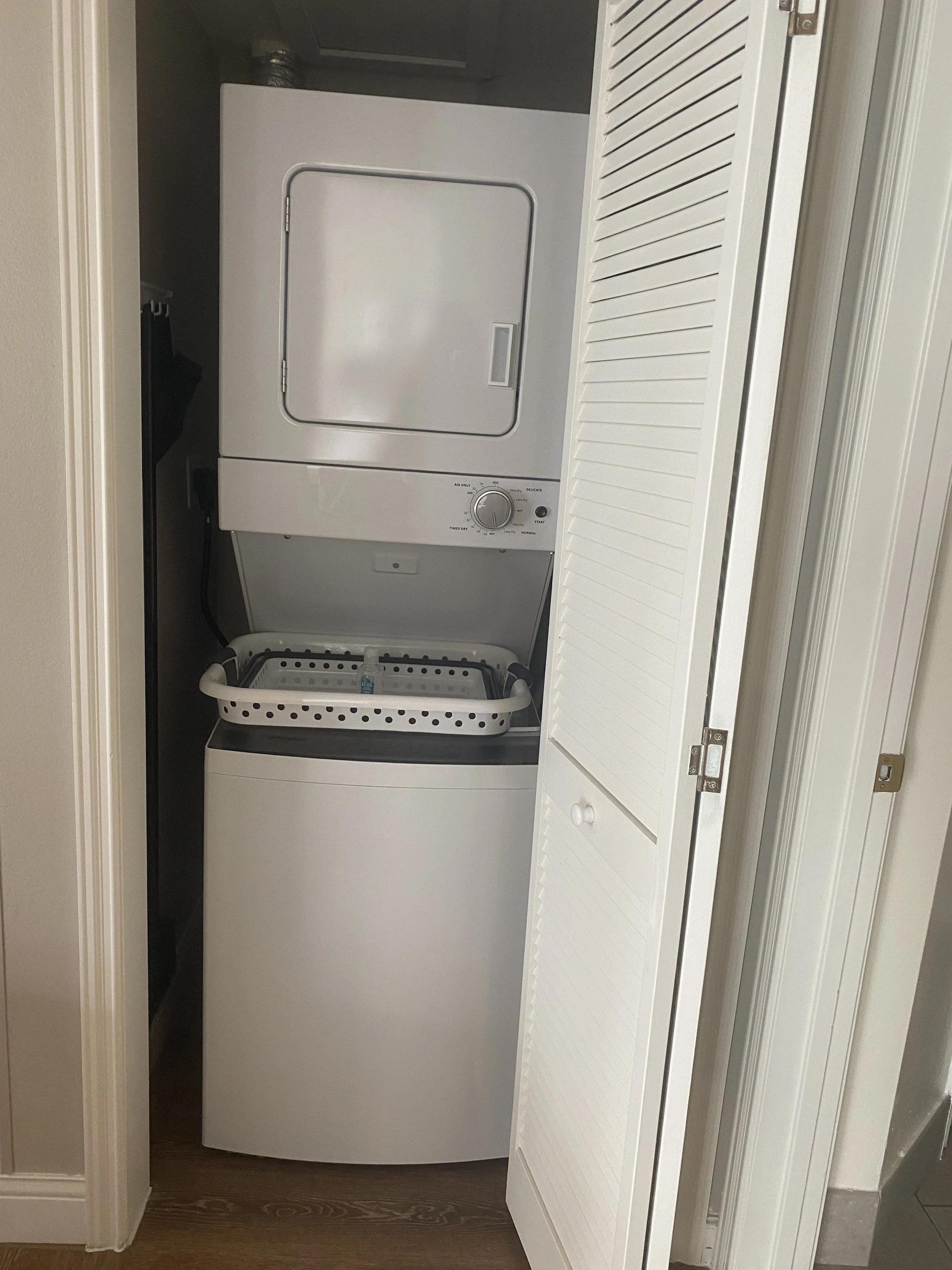 A stacked washer and dryer unit inside a closet with louvered door.