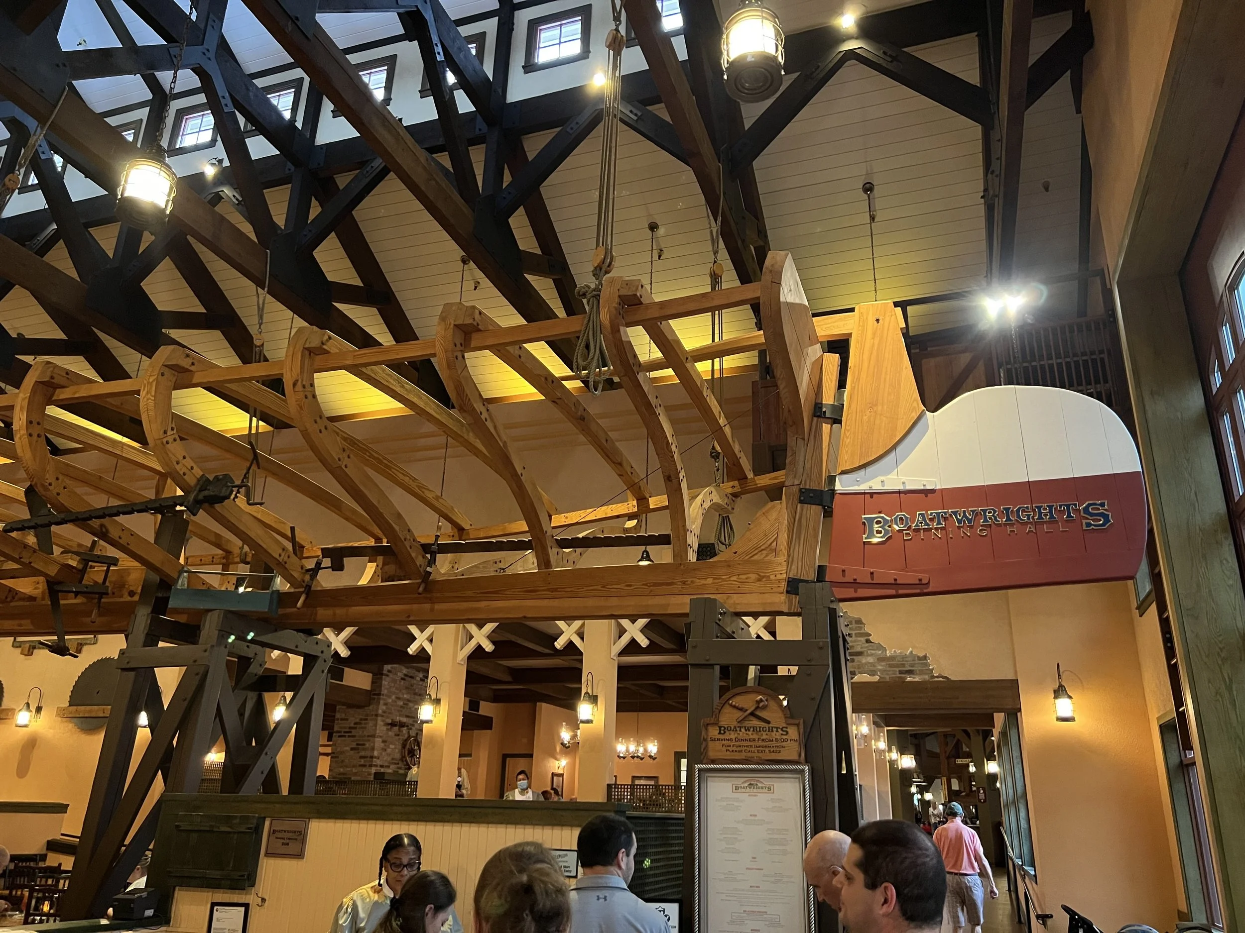 Interior of a restaurant with a large boat-shaped wooden structure suspended from the ceiling, with visible people and a menu in the foreground.