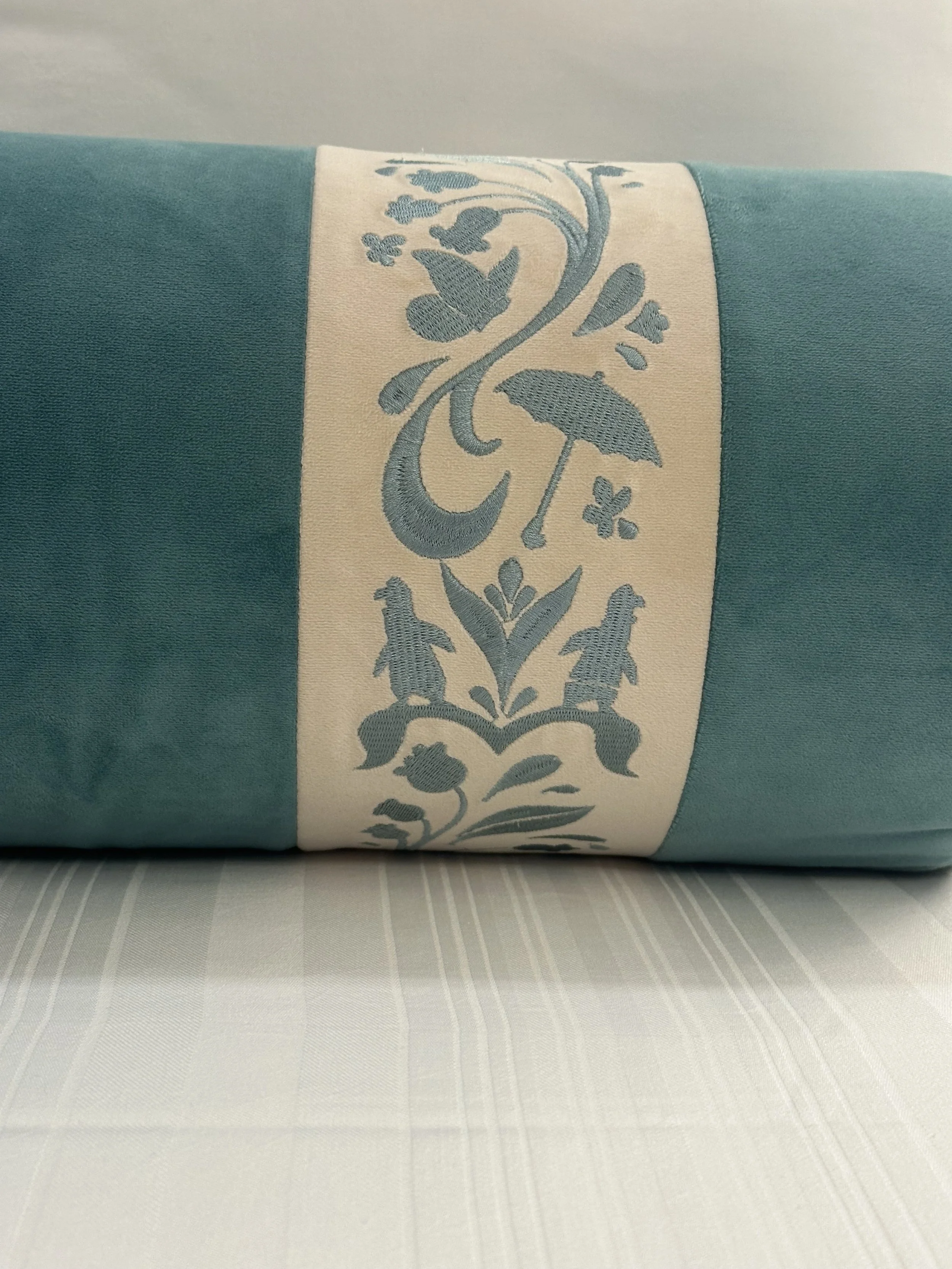 Close-up of a rolled turquoise tablecloth with a white and light blue embroidered floral and animal pattern strip.