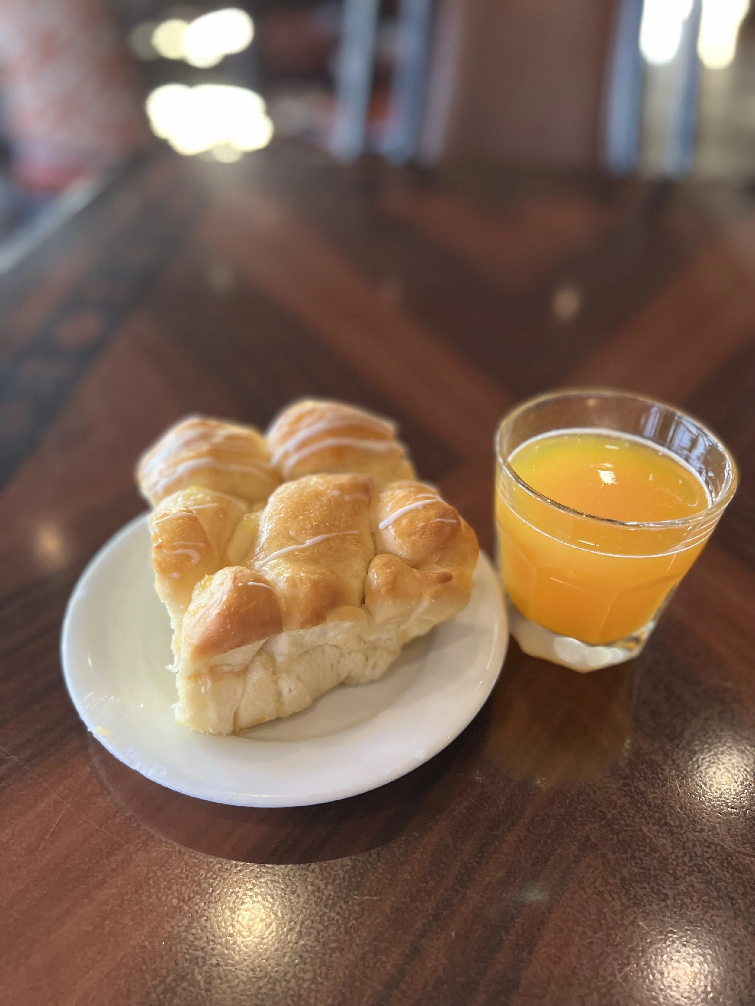A plate with a slice of apple cinnamon swirl bread and a glass of orange juice on a wooden table.