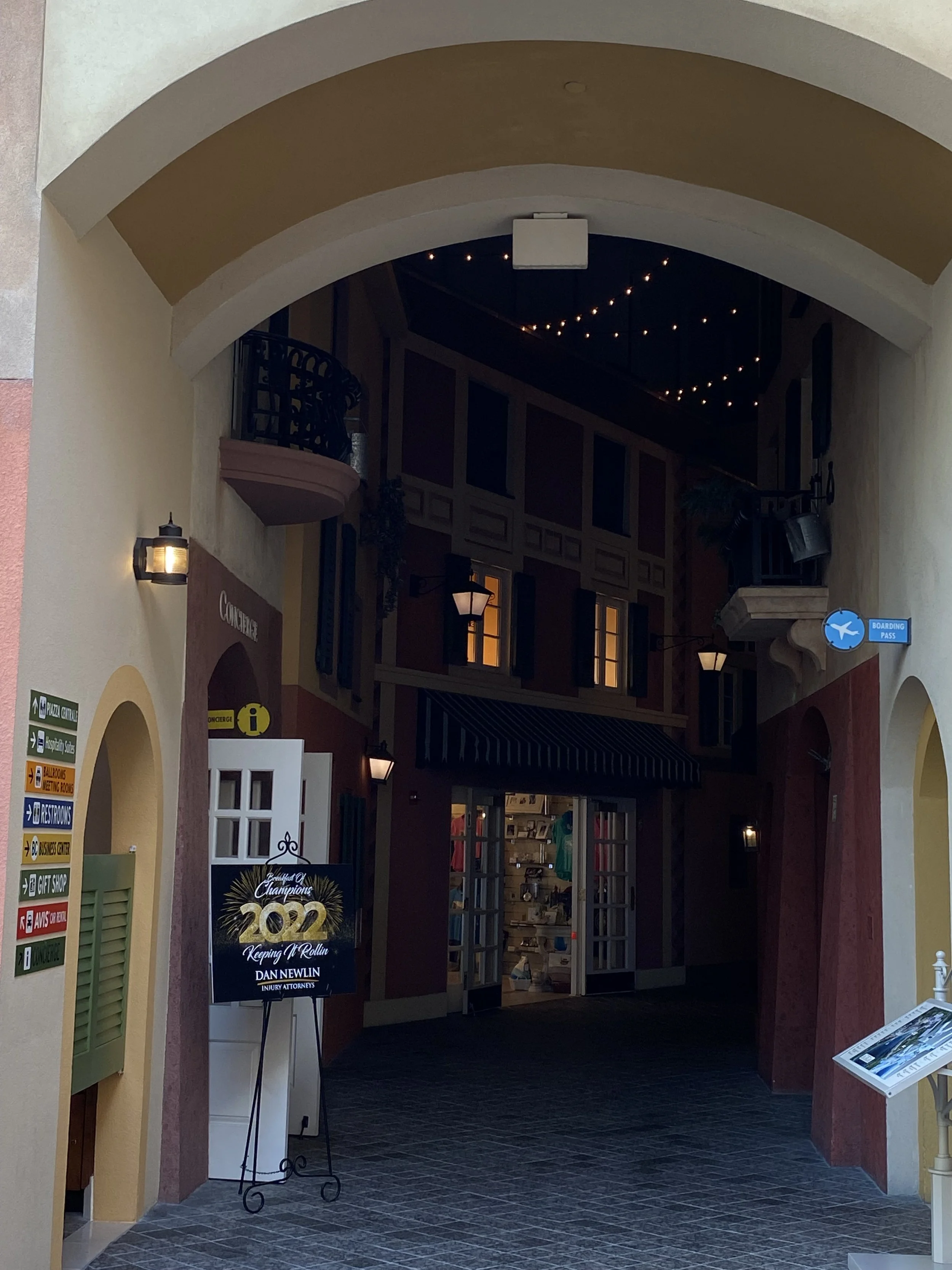 Indoor shopping area with signage, stores, and decorative lighting.