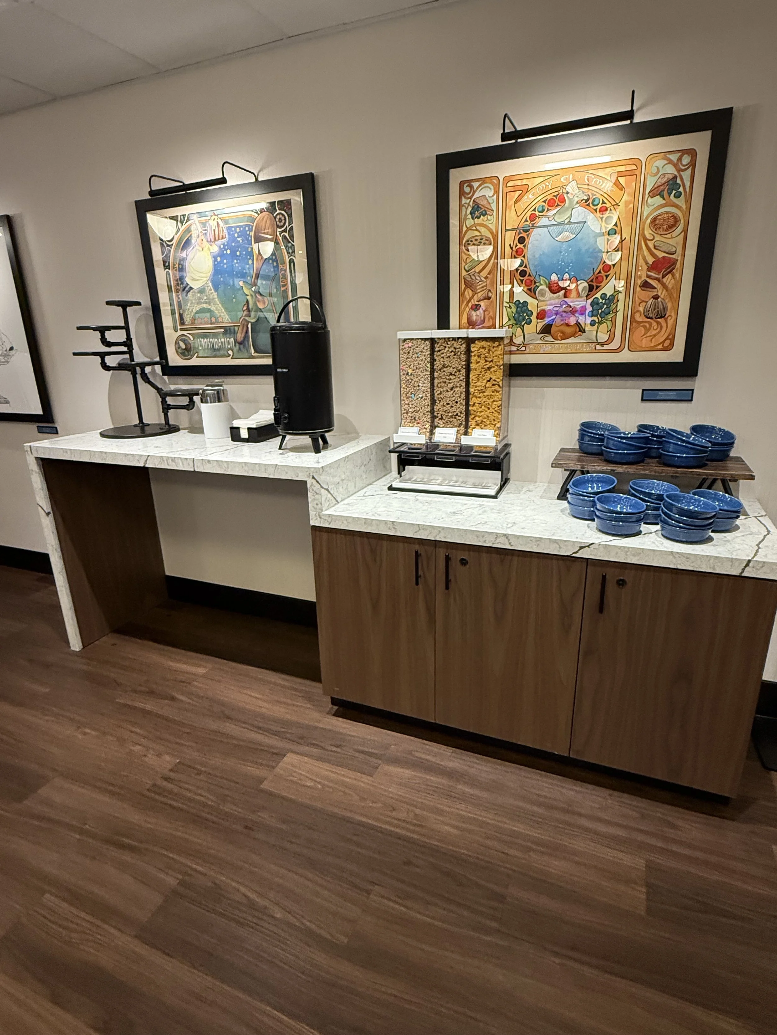 Breakfast buffet area with cereal dispensers, bowls, and artwork on the wall.