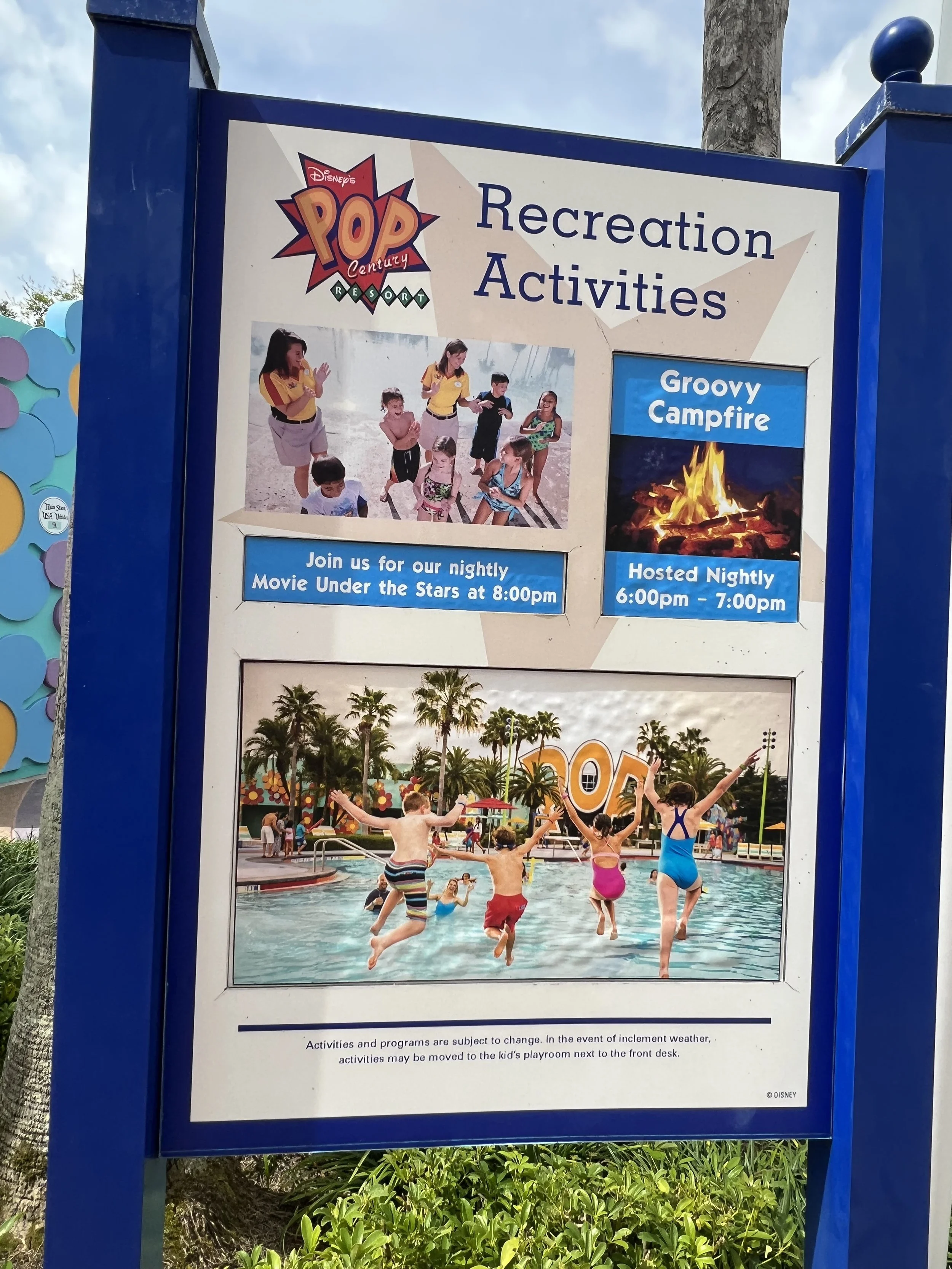 Signboard with information about recreation activities at Disney's Pop Century Resort, including a photo of children playing in a pool, a picture of a campfire, and group of kids jumping into the pool.