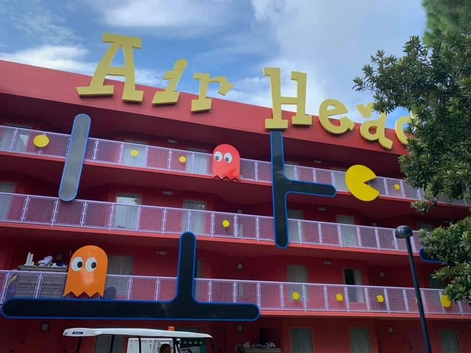 Colorful building with large yellow letters spelling 'Air Head' on top, decorated with Pac-Man characters and Tetris shapes, against a partly cloudy sky.