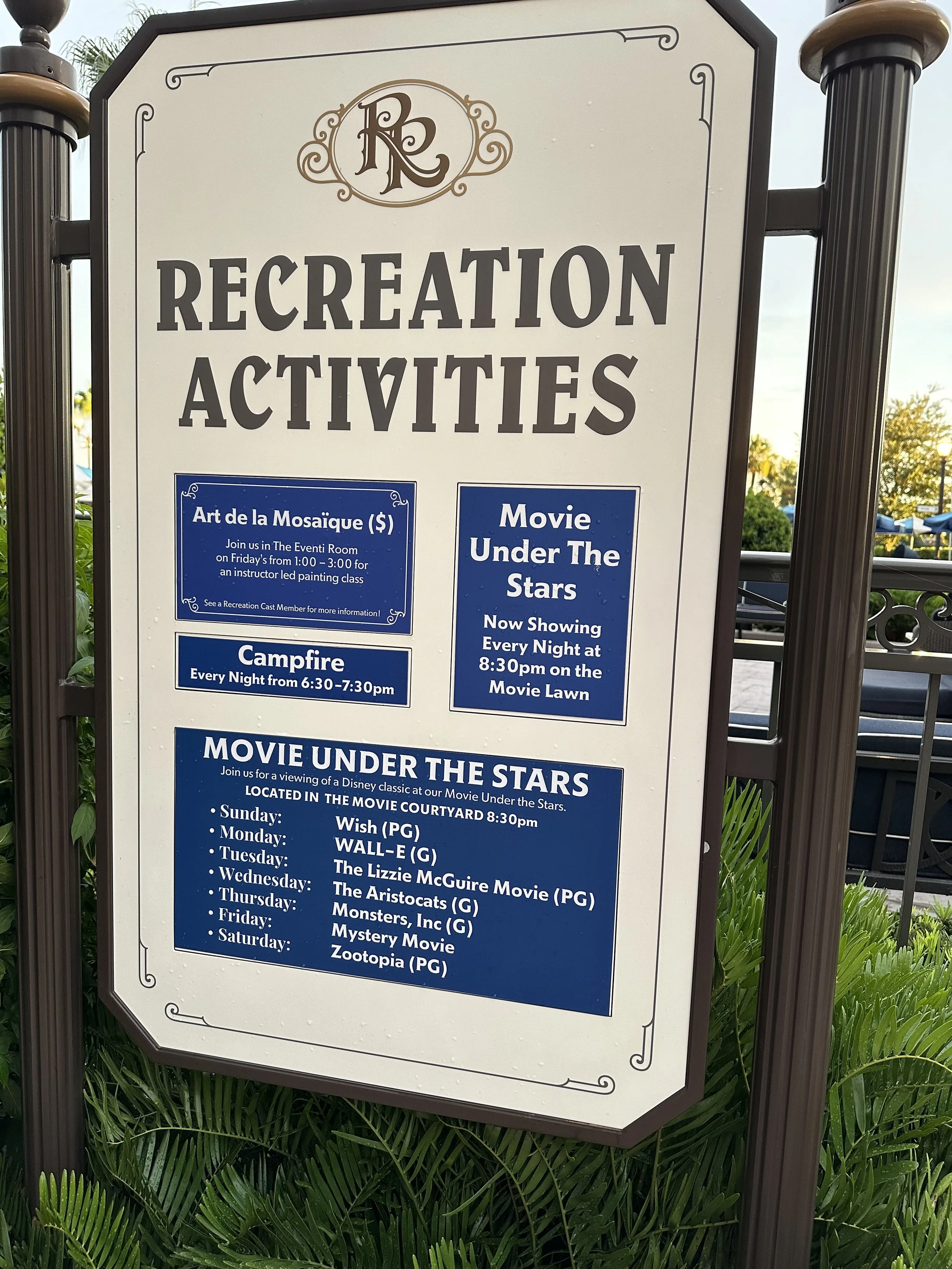 Signboard listing recreation activities including mosaic art classes, campfire nights, and nightly movies under the stars at the Movie Lawn, with a schedule of Disney movies playing on different days.