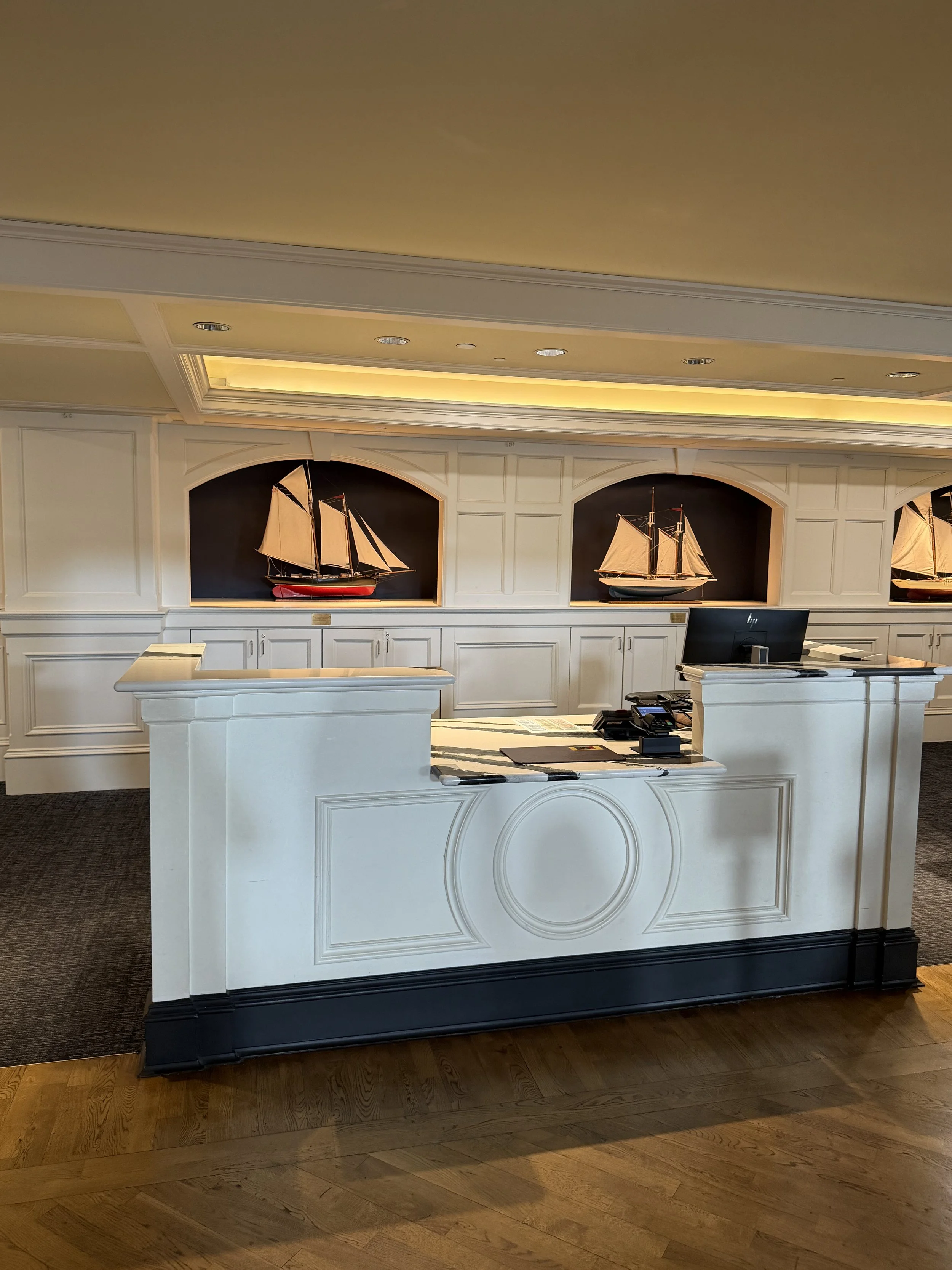 Hotel reception desk with three model ships displayed in wall niches behind it.