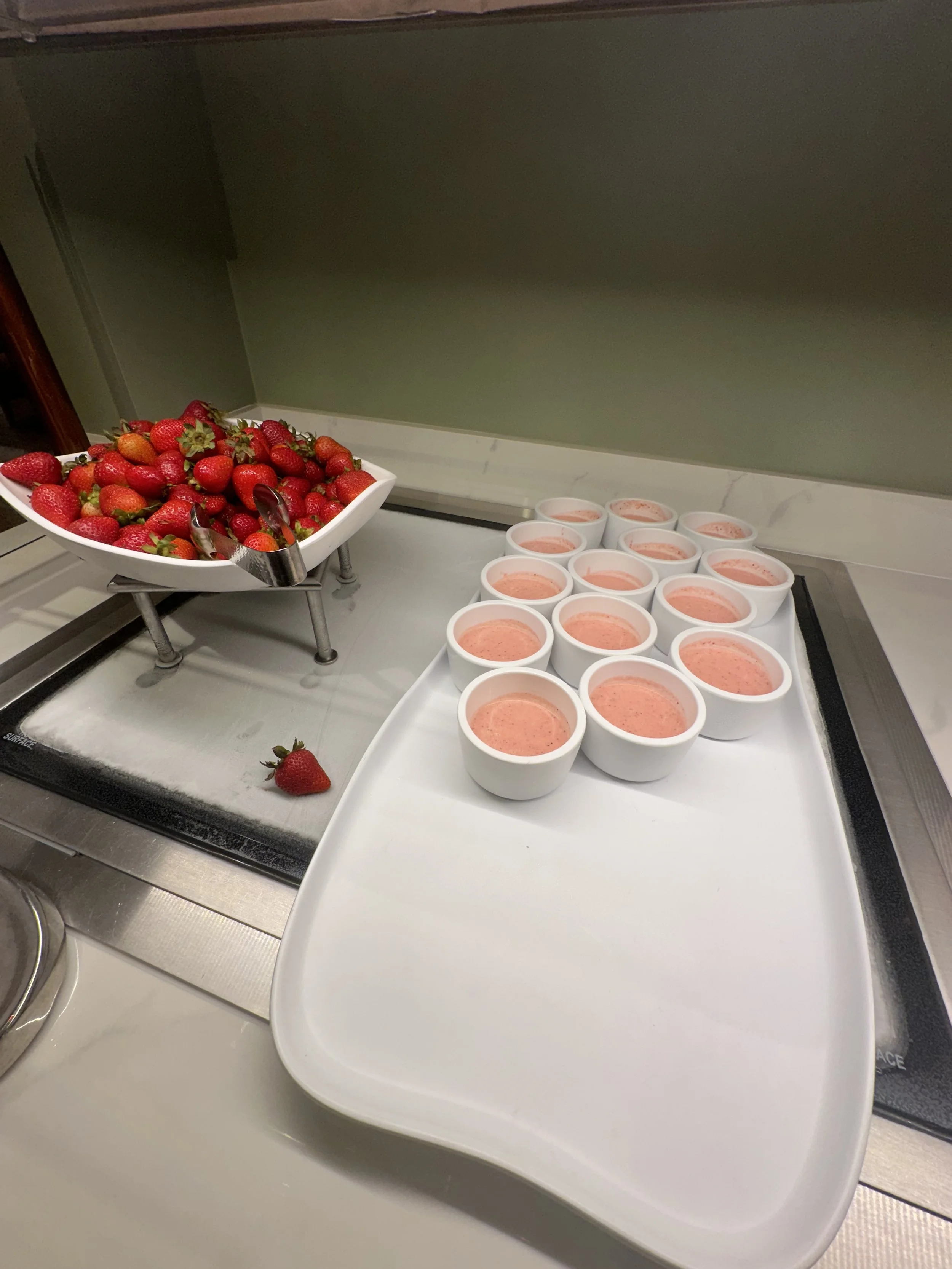 Tray of pink fruit smoothies and a bowl of fresh strawberries with tongs.
