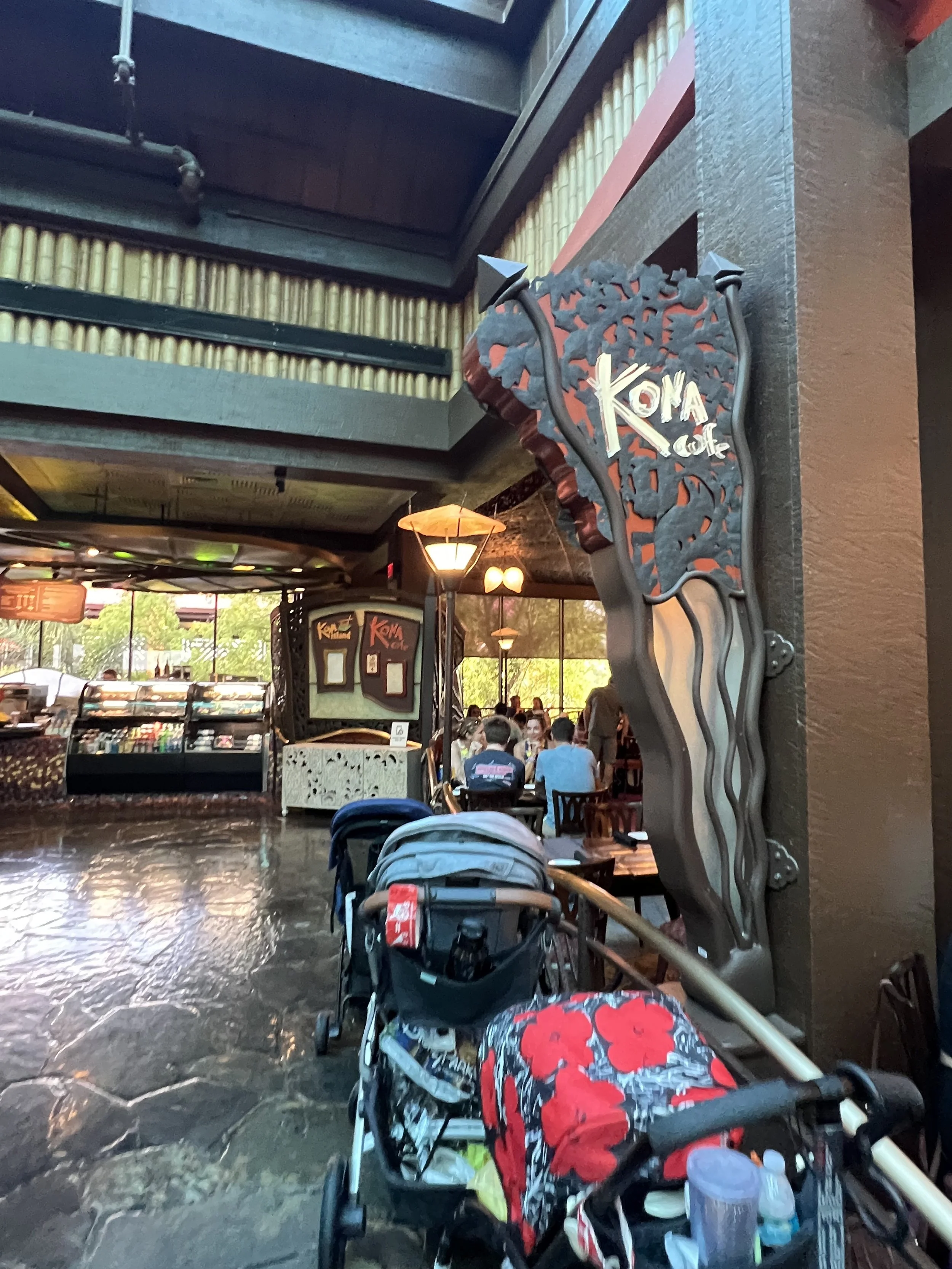 Interior of Kona Cafe with a sign on the wall, people dining at tables, and strollers parked in the foreground.