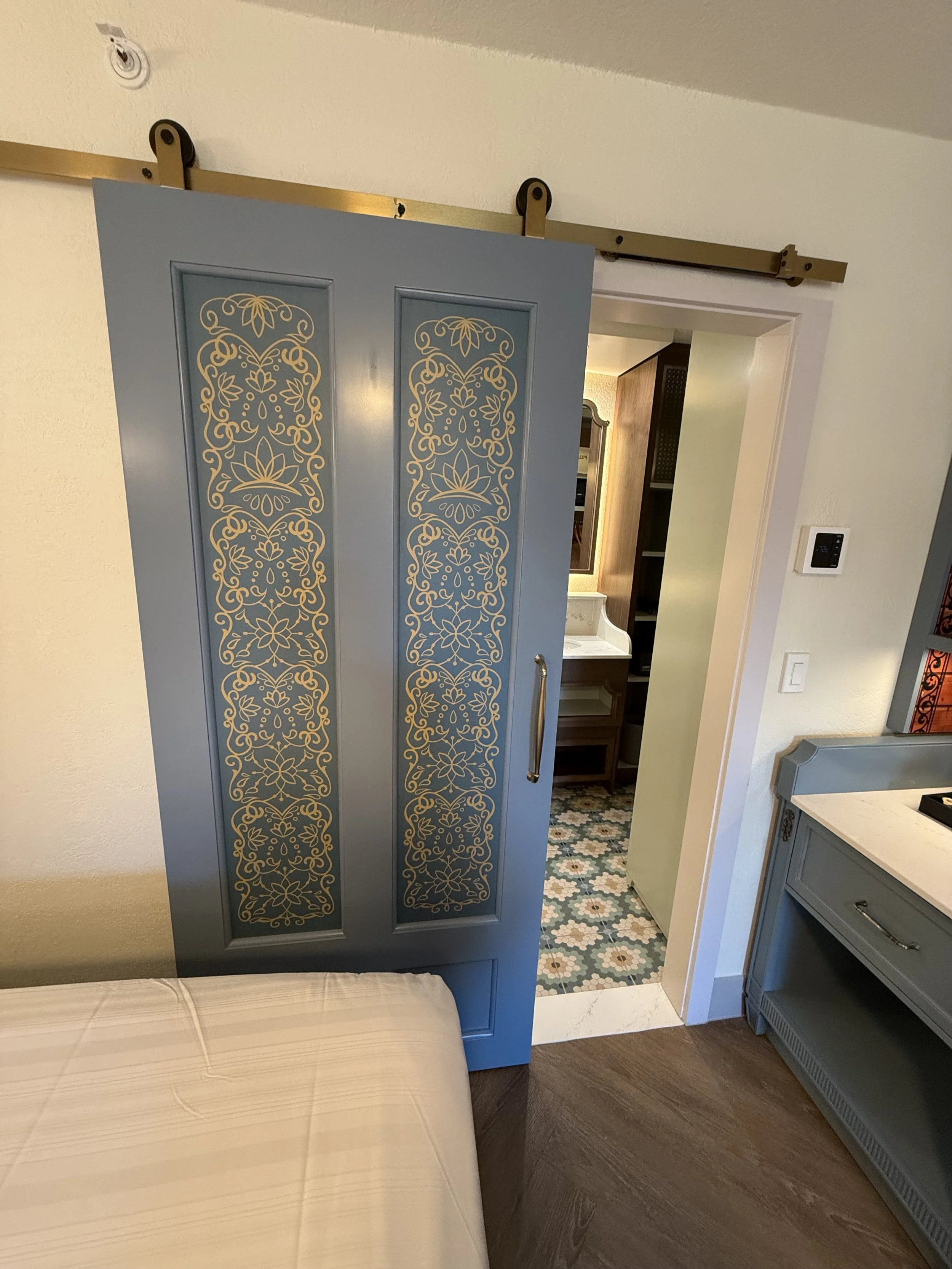 Blue sliding door with ornate gold patterns, partially open to reveal a bathroom with patterned tile floor and wooden cabinets.