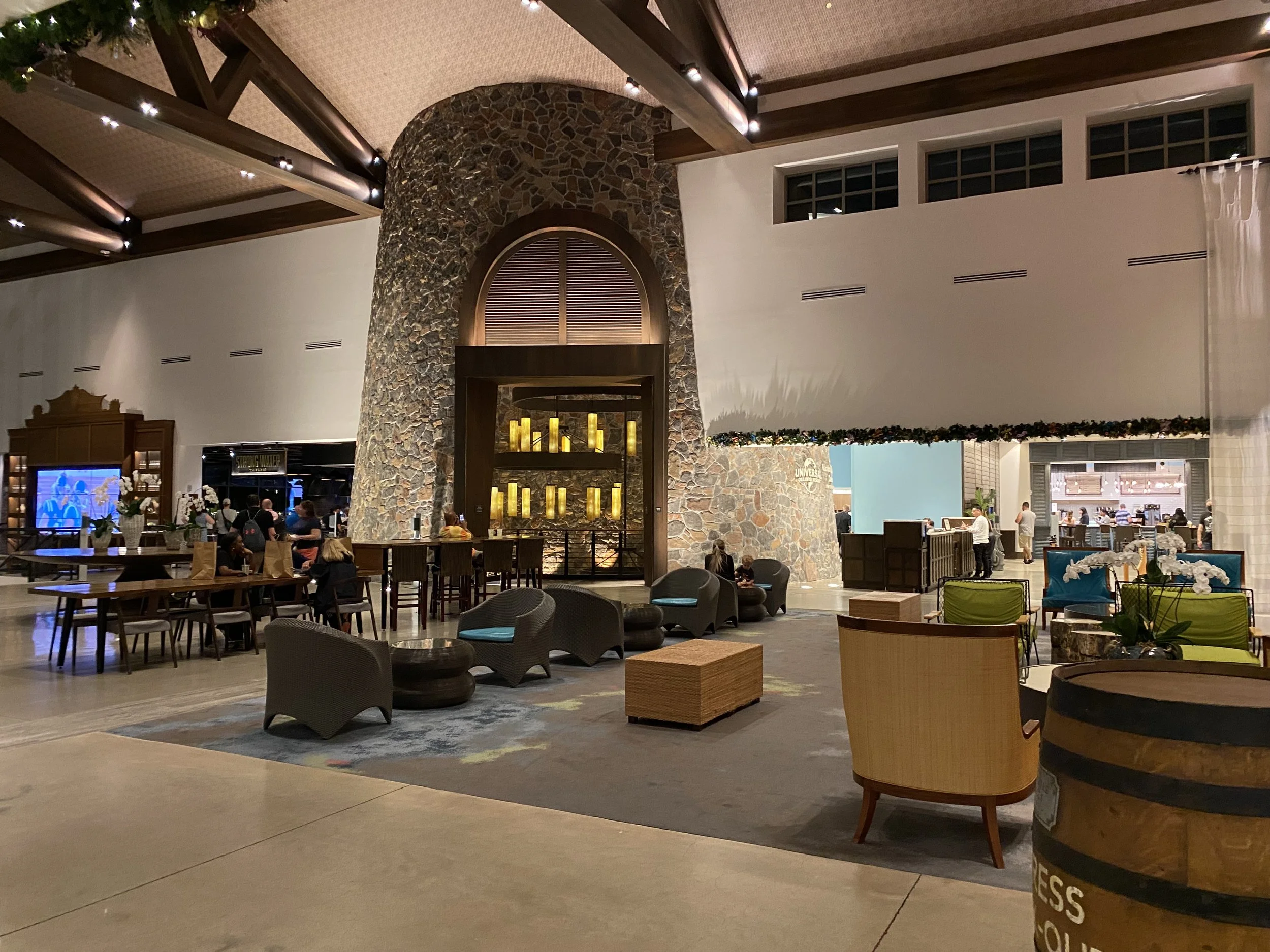 Hotel lobby with seating area, stone fireplace, bar counter, and a barista station, decorated for the holidays with flowers and garland, during evening.