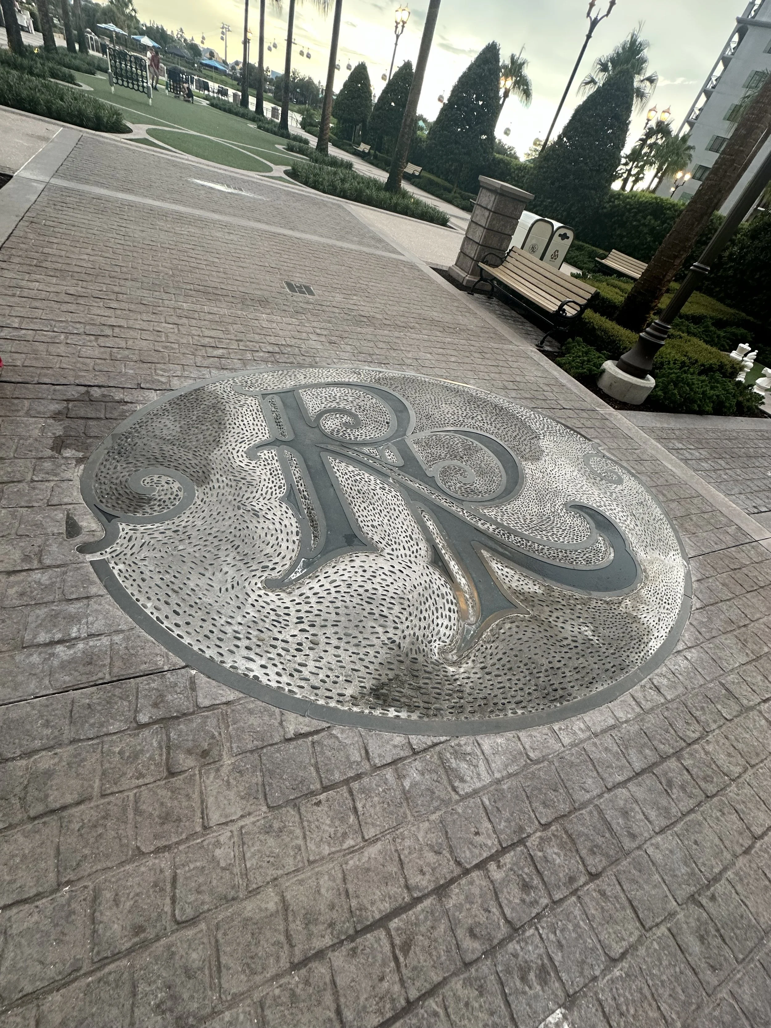 A decorative metal cover with an ornate design is embedded in the brick sidewalk.