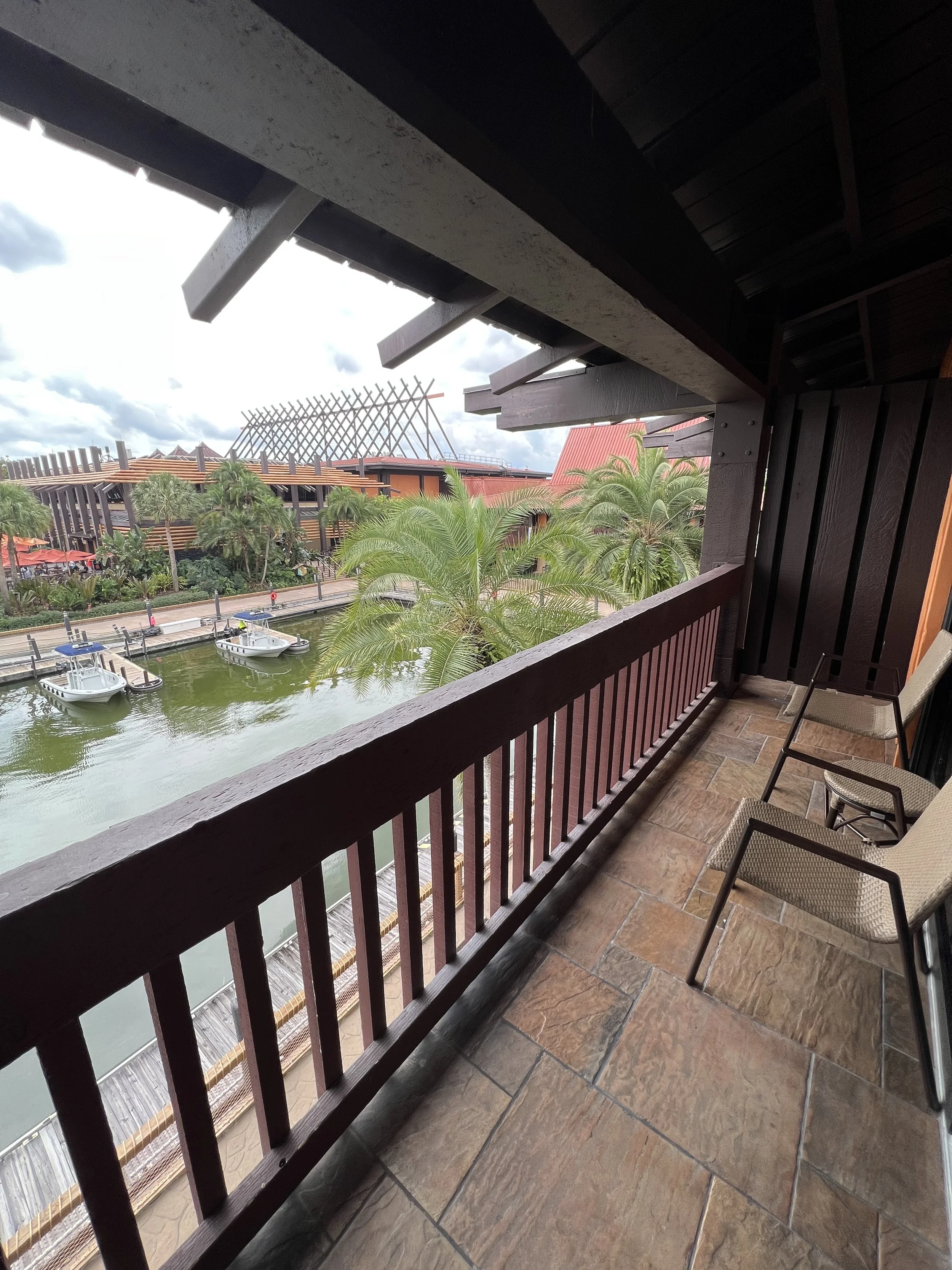 View from a balcony over a waterway with boats, palm trees, and buildings with modern architecture in the background.