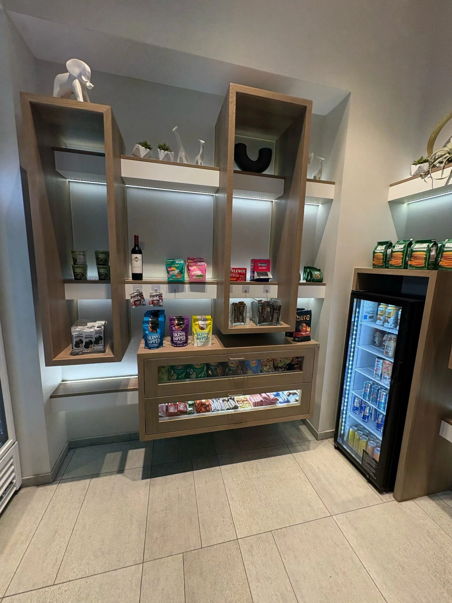 Snack and beverage display in a convenience store with a glass-door refrigerator, snack shelves, and decorative items on top.