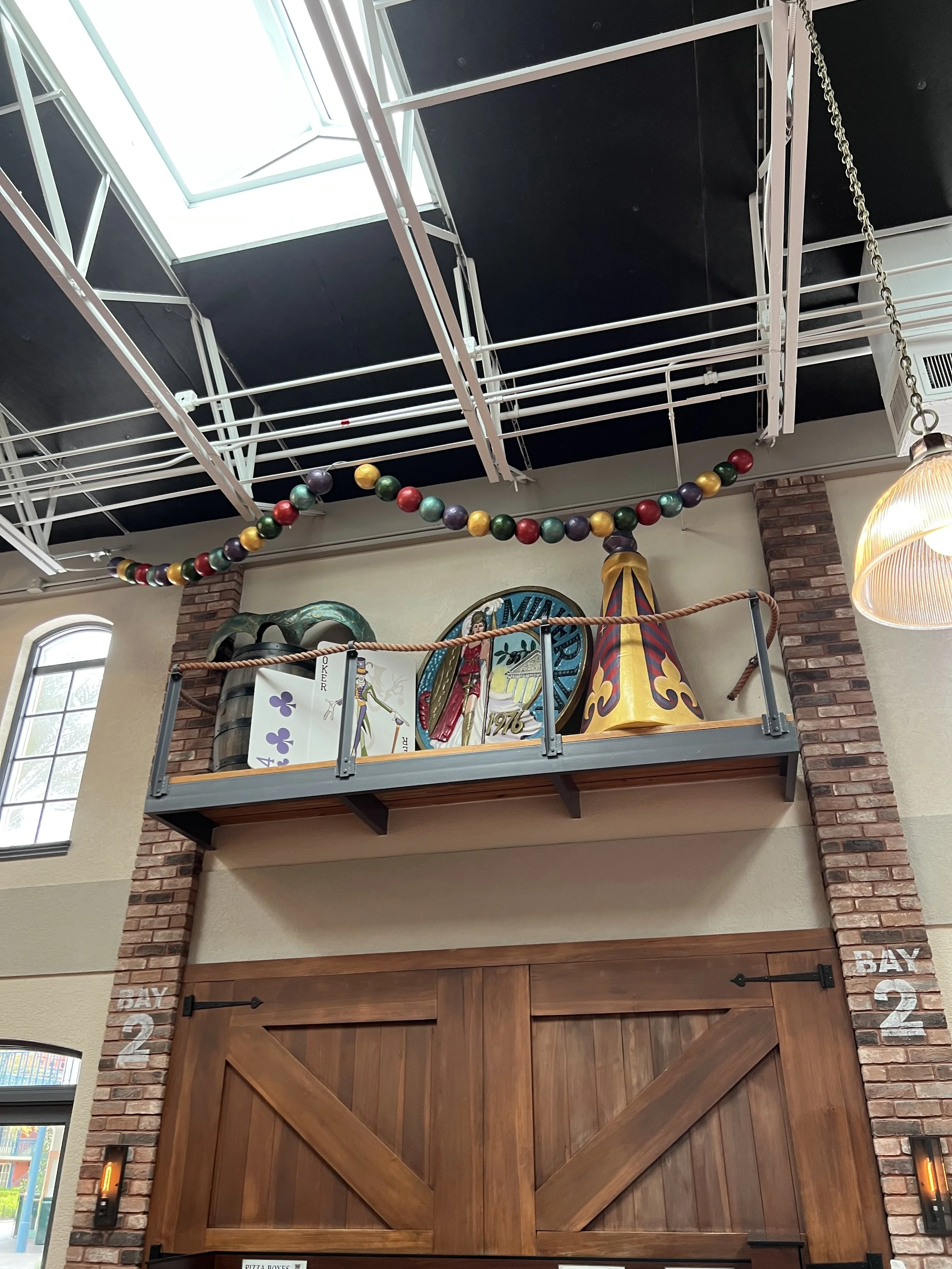 Decorative display on a ledge with a treasure chest, a sign with a skeleton playing golf, a circular sign, and a cone-shaped object, above a wooden barn-style door in a restaurant or cafe.