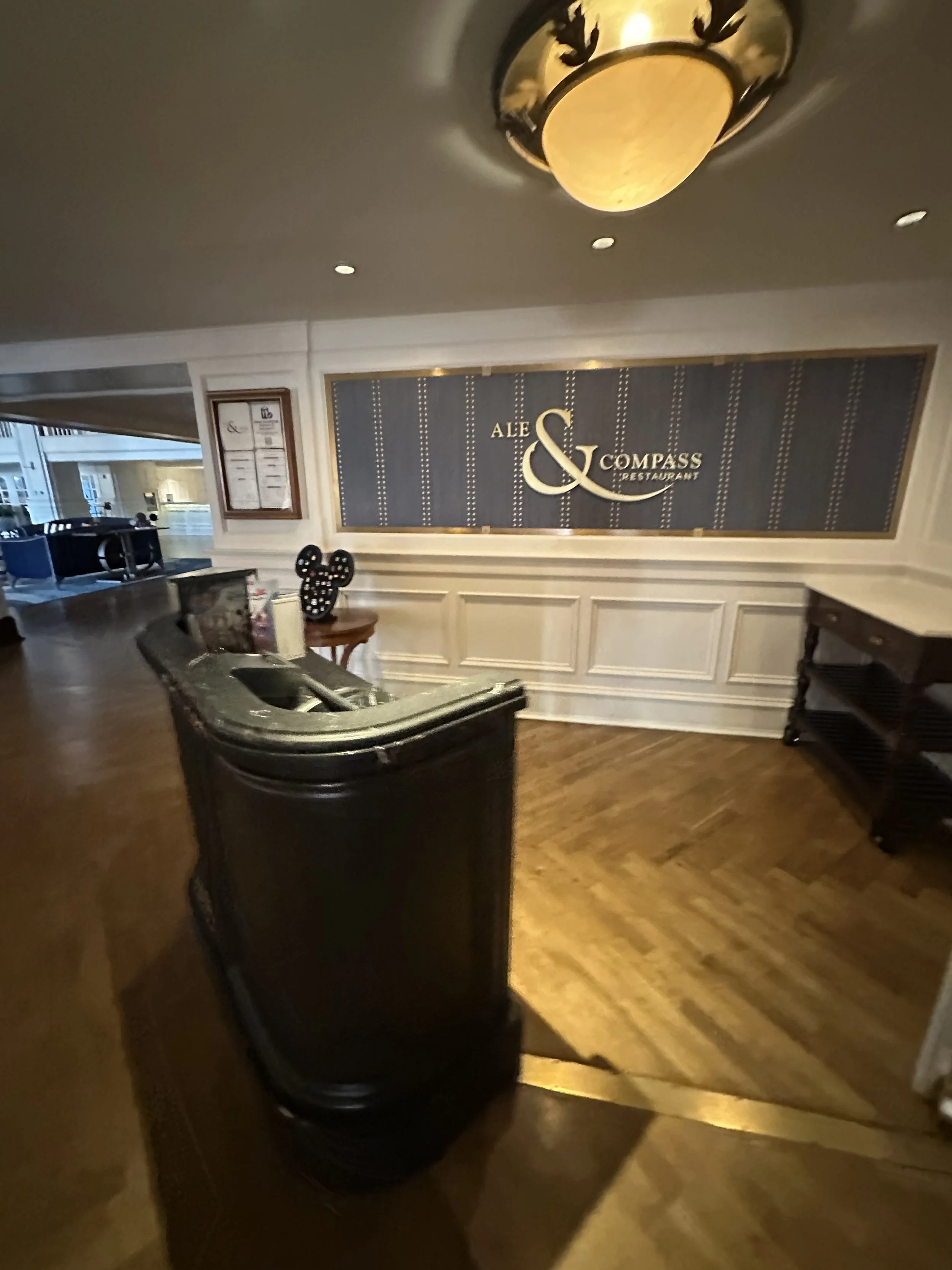 Hotel lobby with a reception desk, wooden flooring, and a large sign on the wall reading 'Alec & Compass Restaurant'.