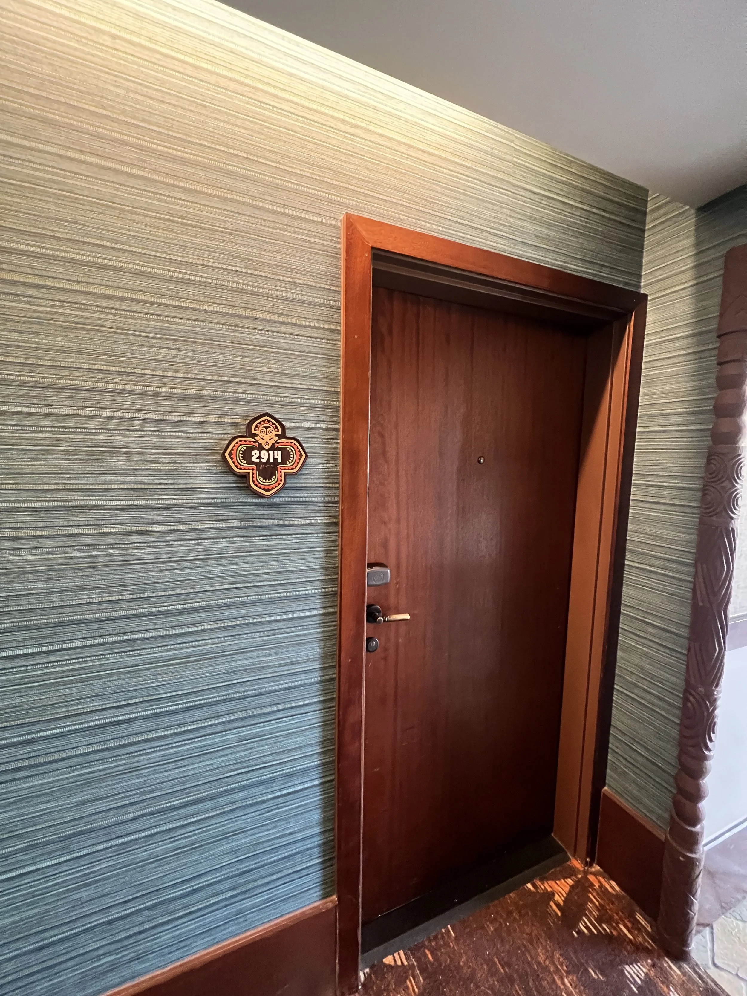 Hotel room door with the number 2914 on a decorative plaque on a textured wallpapered wall.
