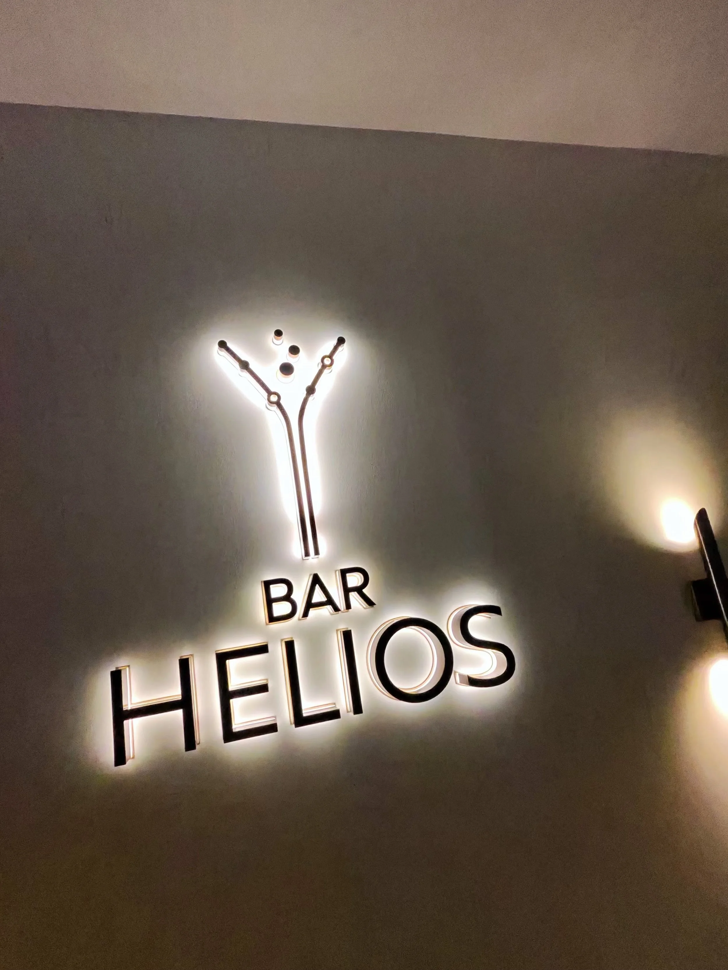 Neon sign for Bar Helios featuring a martini glass illustration and illuminated text on a wall.