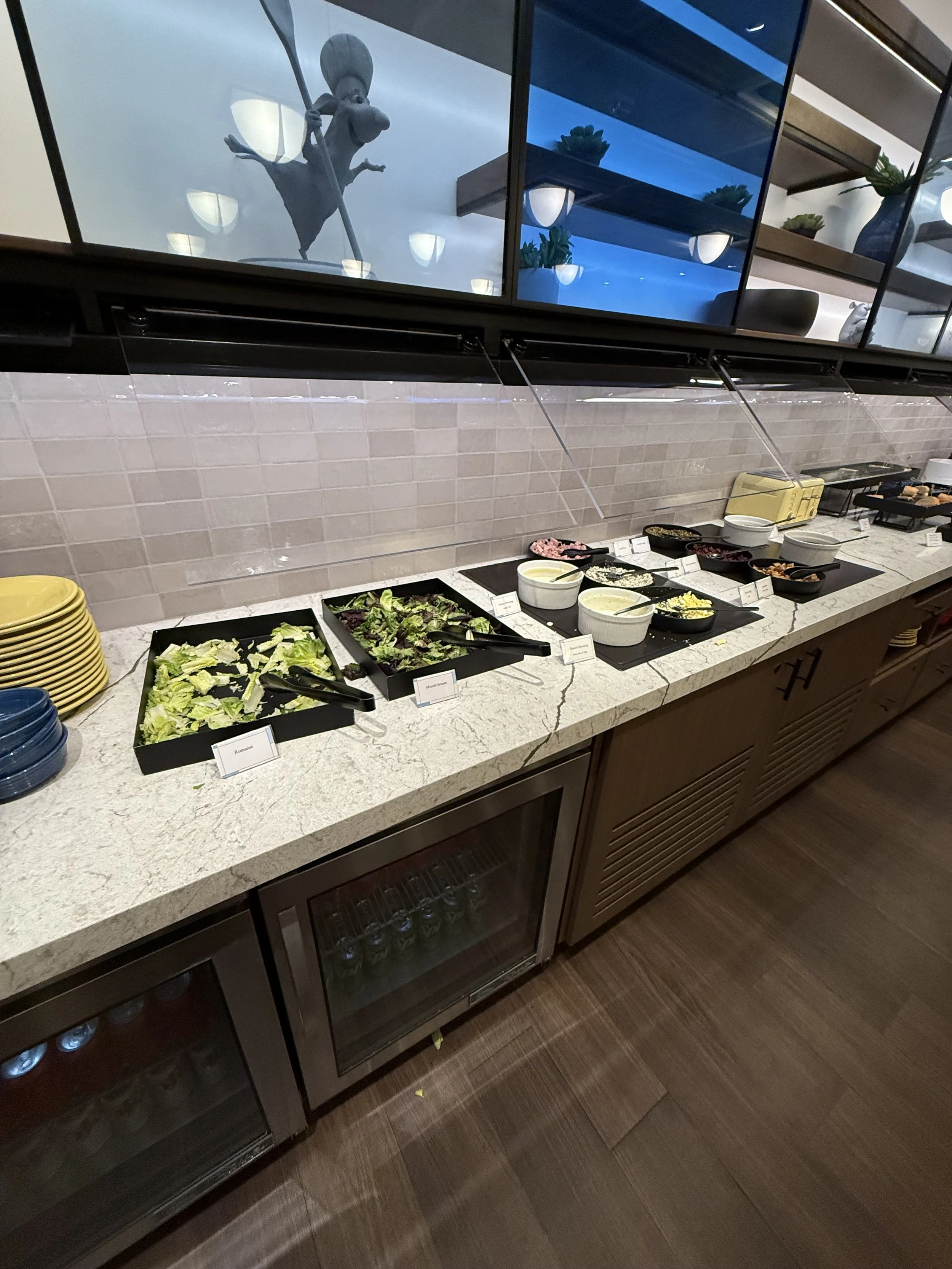 A buffet counter with various salads and condiments, including lettuce, salad greens, and dressings, in a restaurant or cafeteria setting.