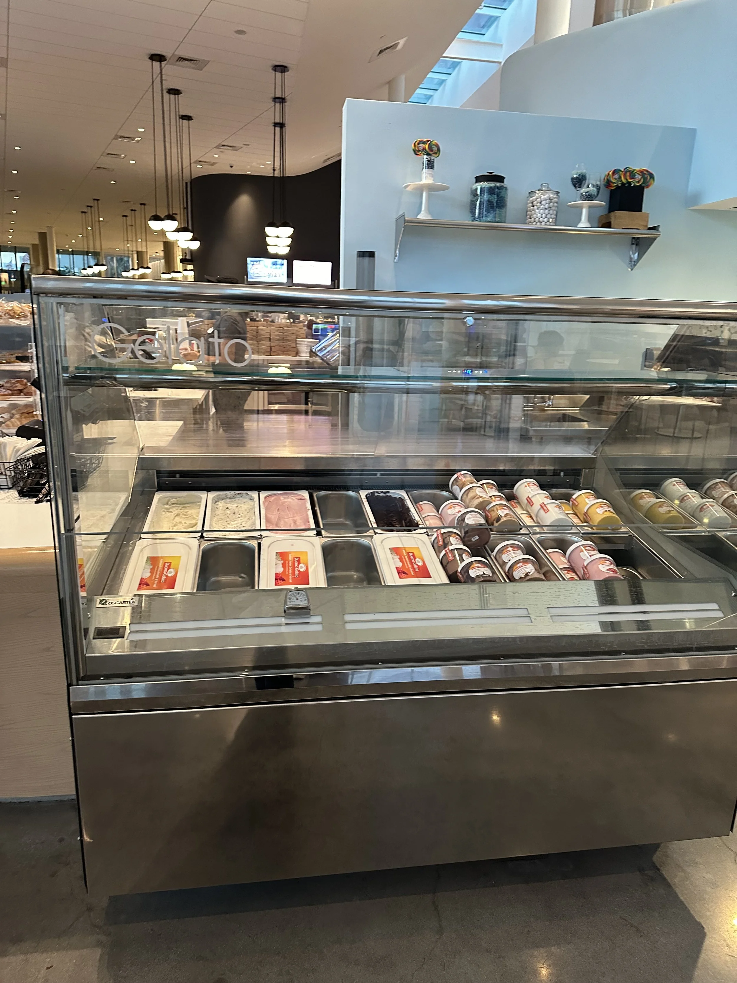 Ice cream freezer display with various flavors of ice cream and gelato in a shopping mall or store.